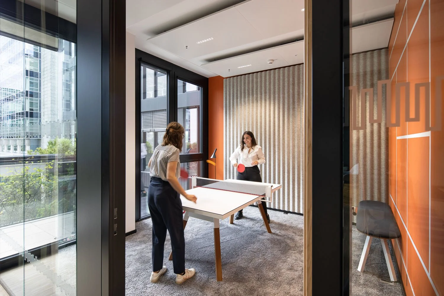 Unternehmensfotografie von einer Office Community Area: Zwei Personen spielen Tischtennis in einem Raum mit Akustikpaneelen.
