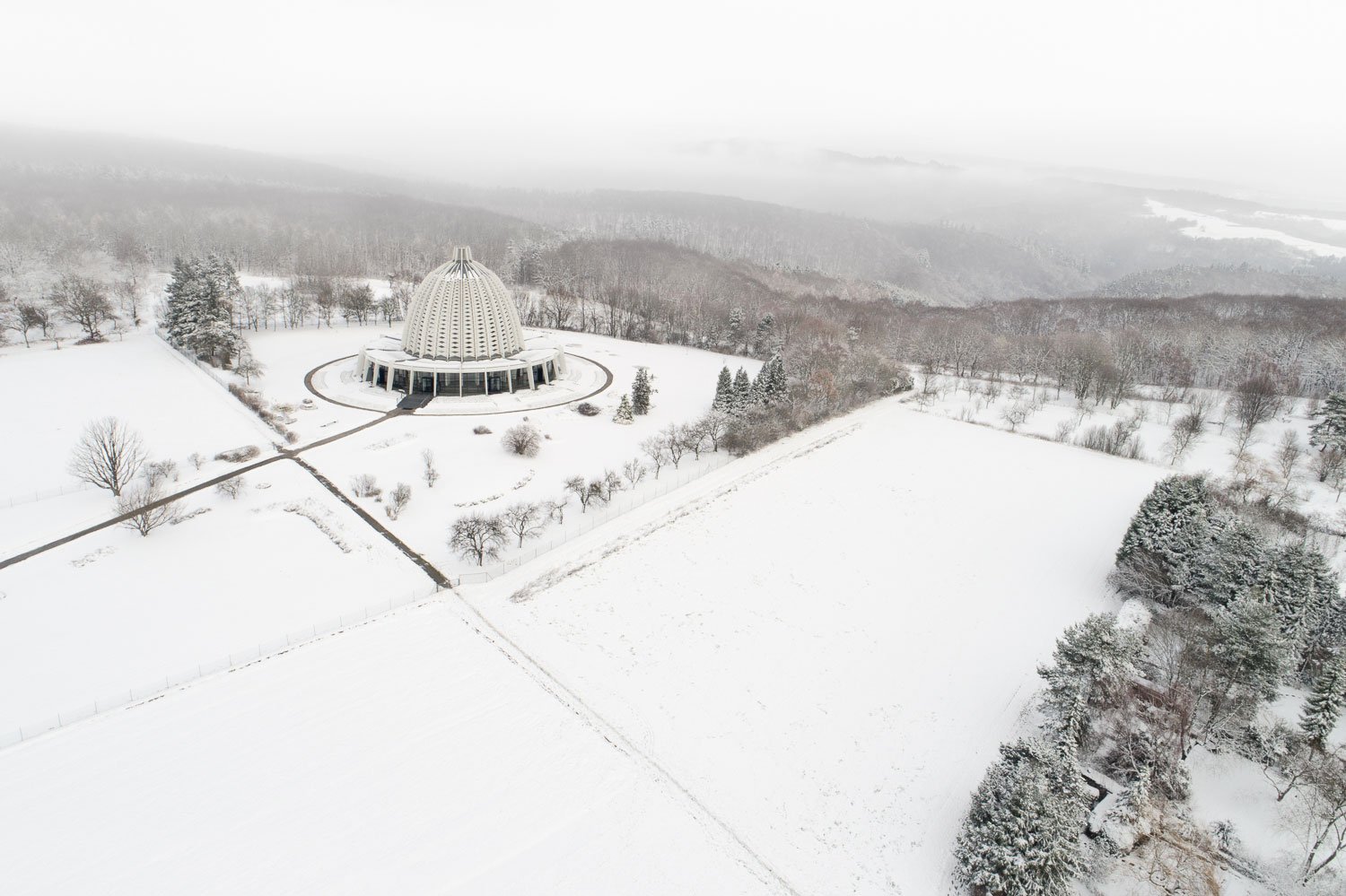 Winterliche Luftaufnahme des Bahá'í-Tempels in Hofheim-Langenhain bei Frankfurt. Die markante Kuppelarchitektur der 60er Jahre fügt sich in die verschneite Mittelgebirgslandschaft des Taunus ein.
