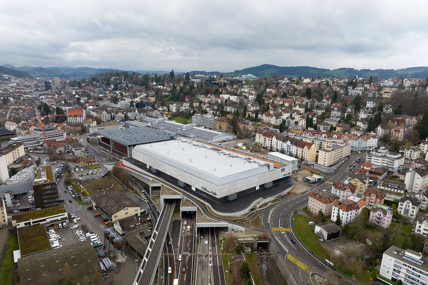 Luftaufnahme der SGKB Halle St. Gallen im städtebaulichen Kontext mit Überdeckung der Autobahn und Messegelände der Olma Messen St. Gallen.

