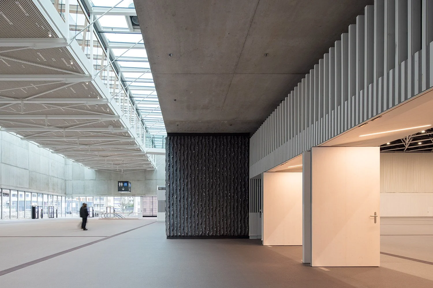 Architekturfotografie des Eingangsbereichs der SGKB Halle St. Gallen mit Betonarchitektur, Lichtdecke und klar gegliederten Raumstrukturen.
