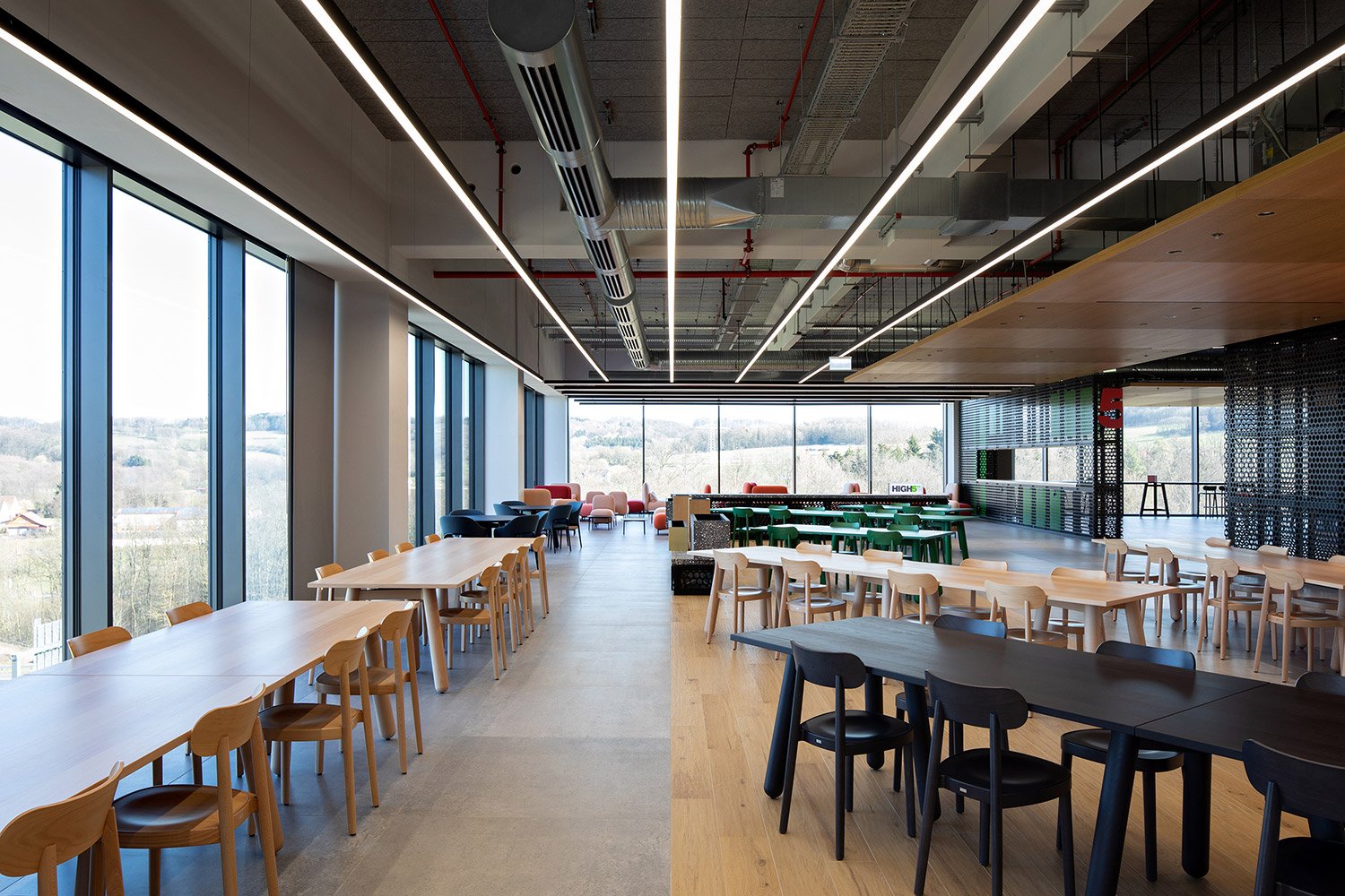 Weitwinkelaufnahme der High5 Mensa in der Engelbert Strauss CI Factory mit langen Tischreihen, raumhoher Verglasung und Thonet-Holzstühlen des Modells 118.
