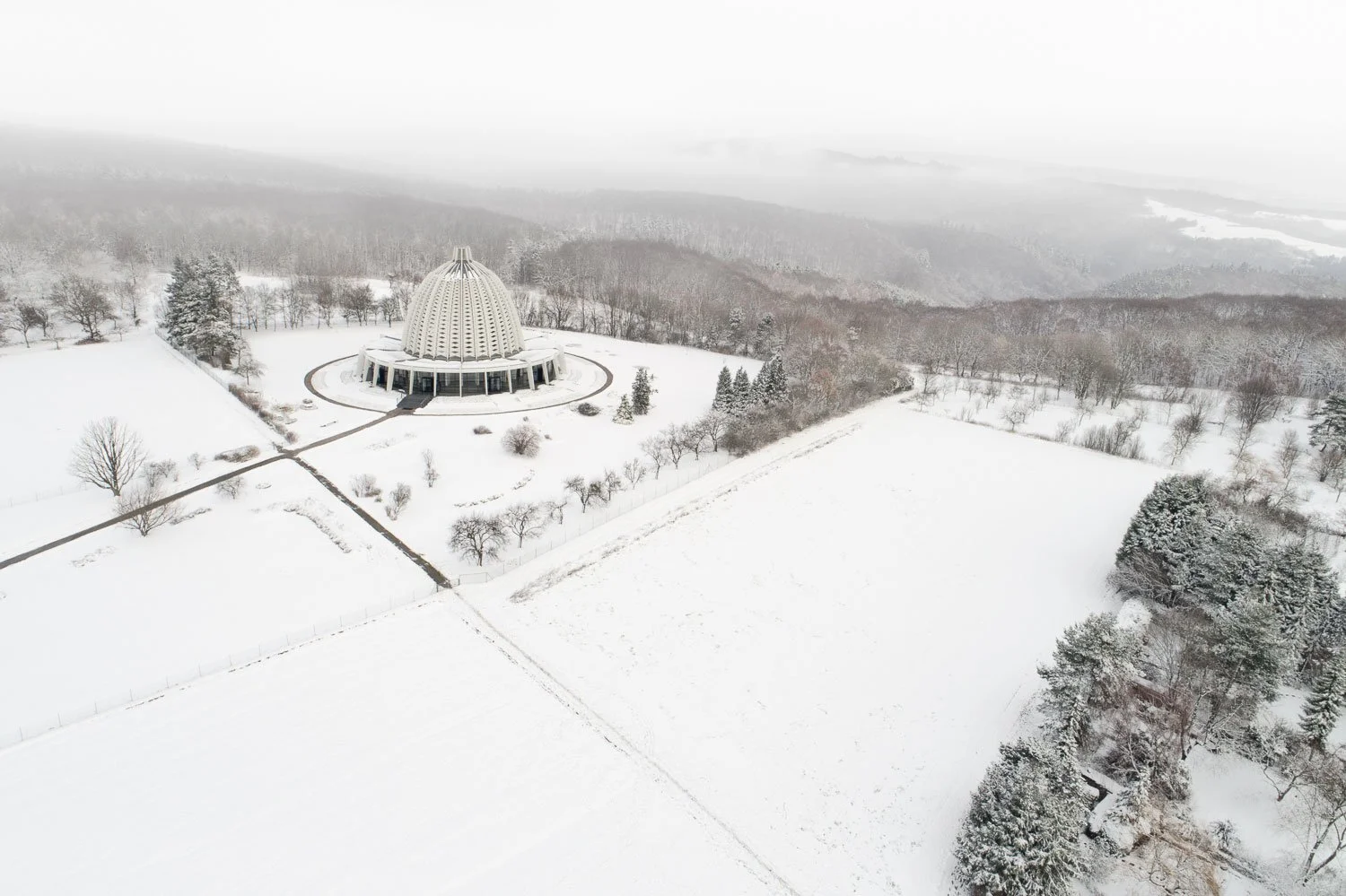 Winterliche Luftaufnahme des Bahá'í-Tempels in Hofheim-Langenhain bei Frankfurt. Die markante Kuppelarchitektur der 60er Jahre fügt sich in die verschneite Mittelgebirgslandschaft des Taunus ein.
