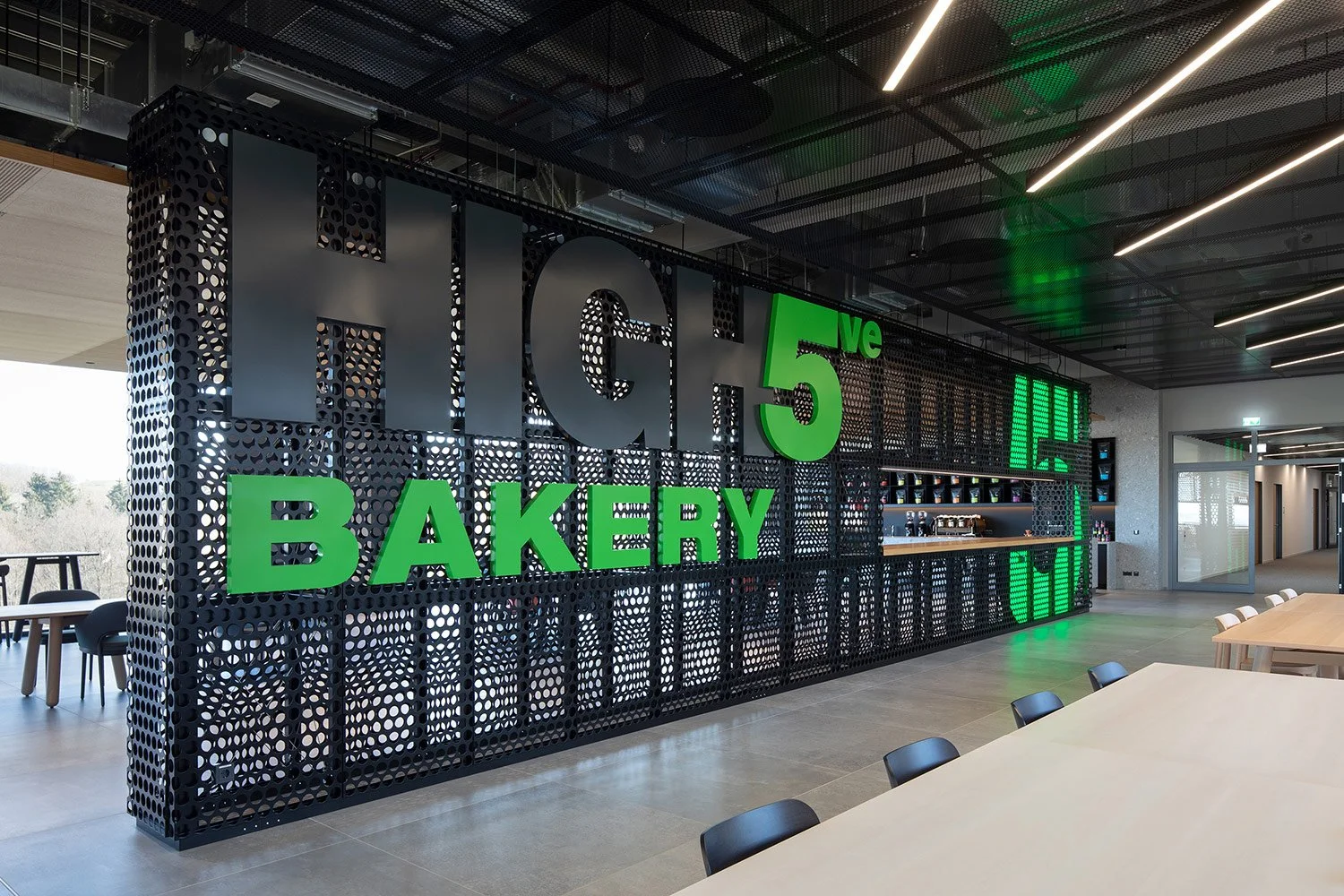Innenraumaufnahme der High5 Bakery in der Engelbert Strauss CI Factory mit perforierten Raumstrukturen, Sitzbereichen und offenem Gastronomiekonzept.

