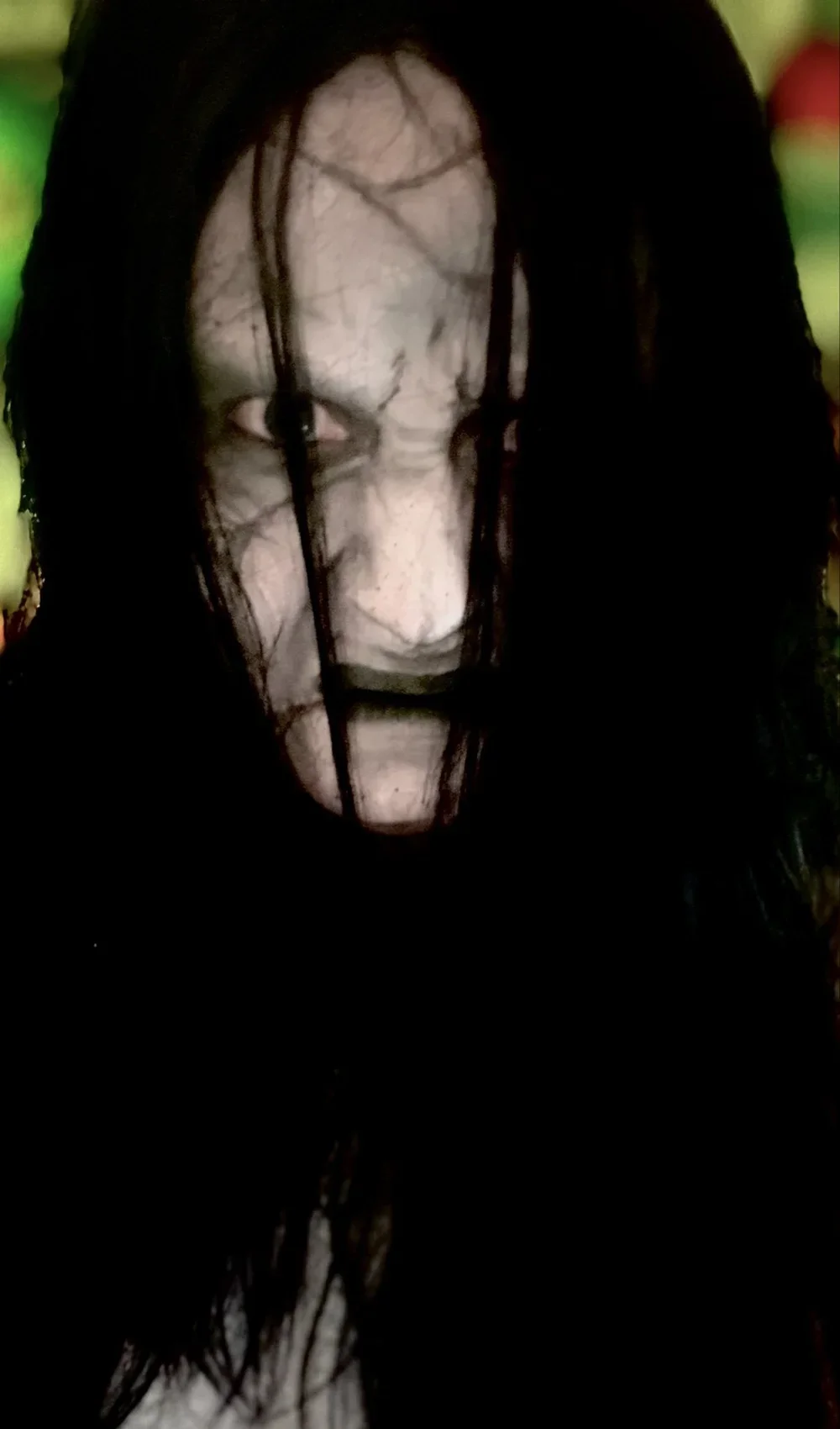 Close-up of a person with long dark hair partially covering their face, with a blurred, abstract background.
