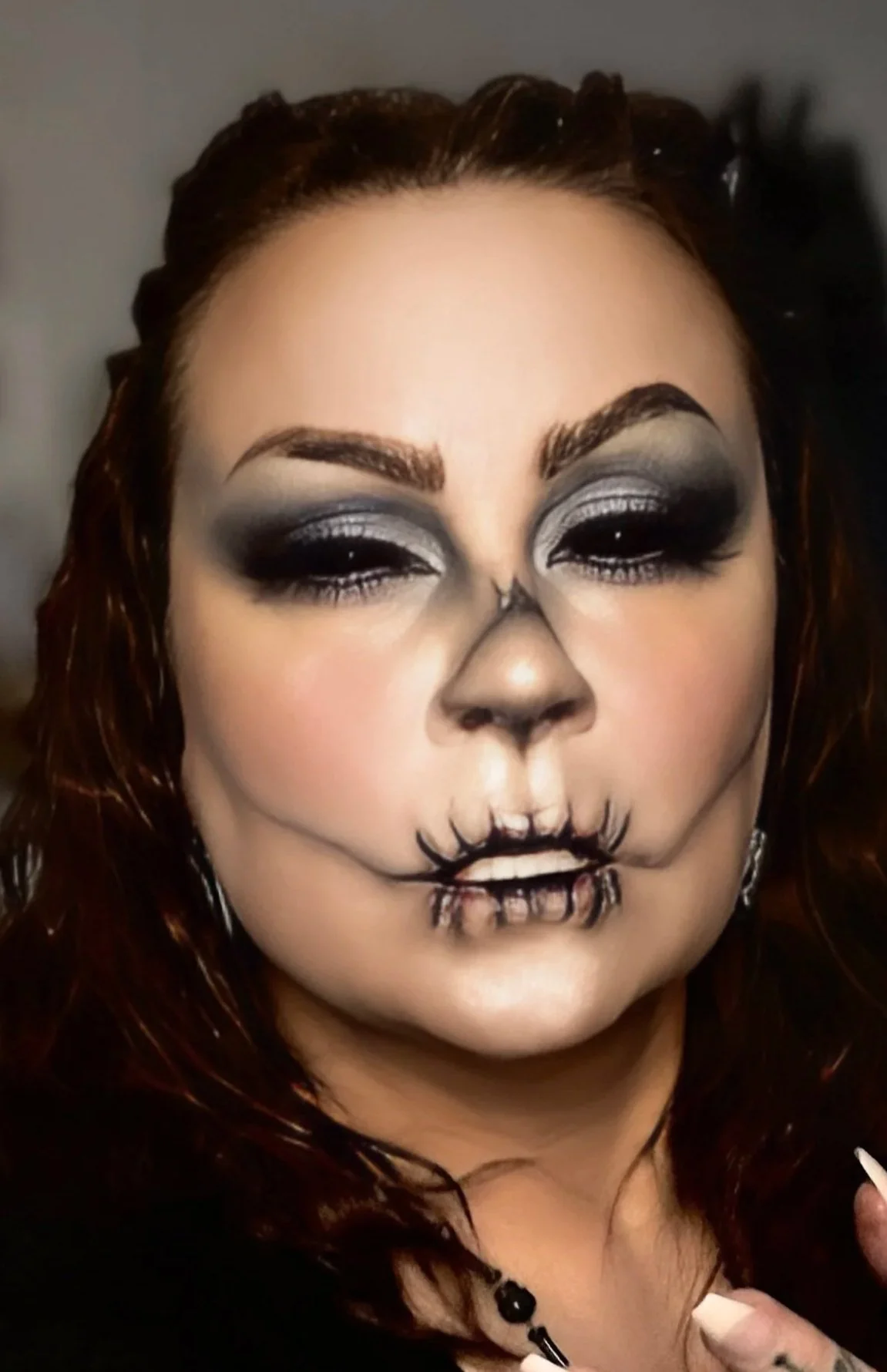 Person with makeup resembling a skeleton, featuring dark eyeshadow, a painted nose, and skeletal teeth design on the lips.