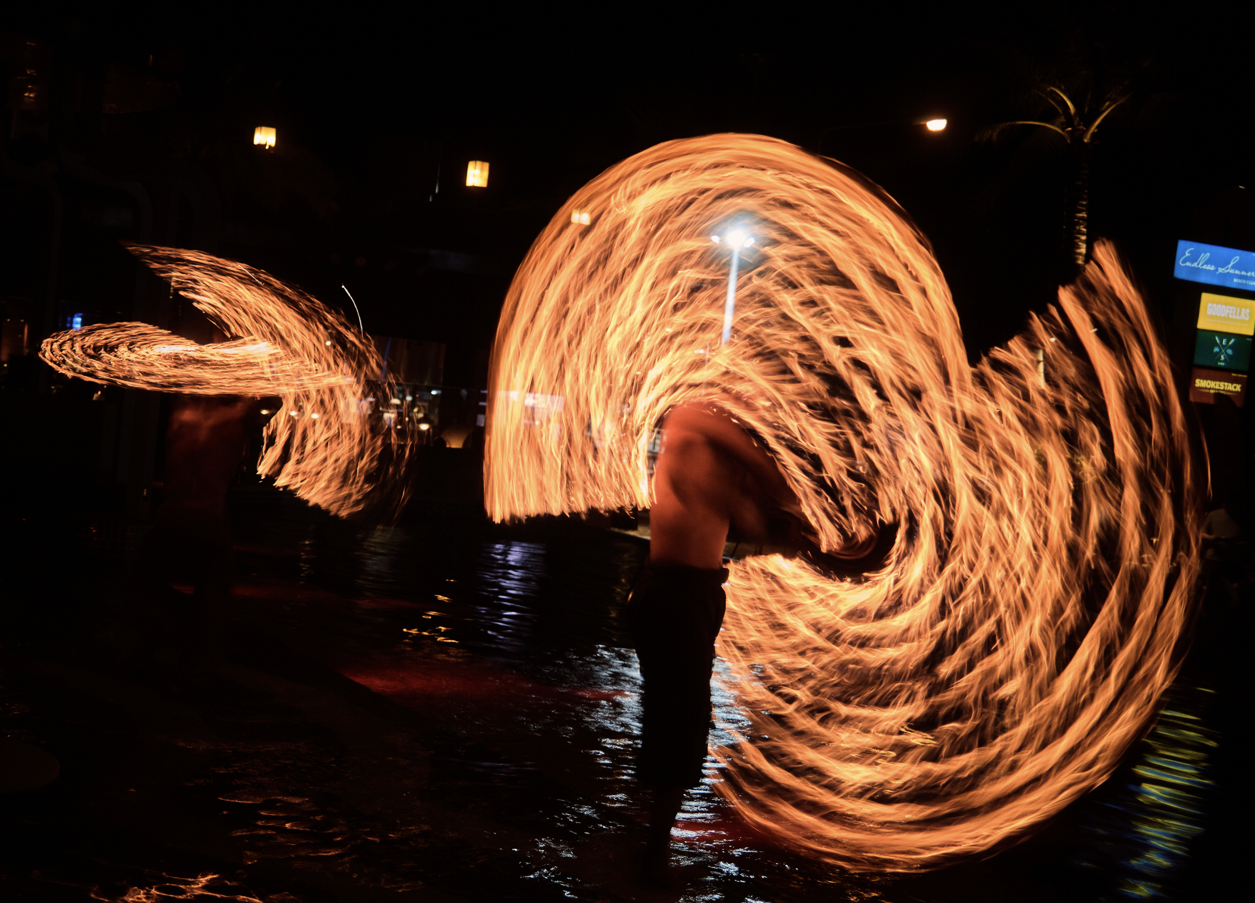 People performing fire dancing or fire spinning at night, creating circular trails of fire with flames. Anemoia.