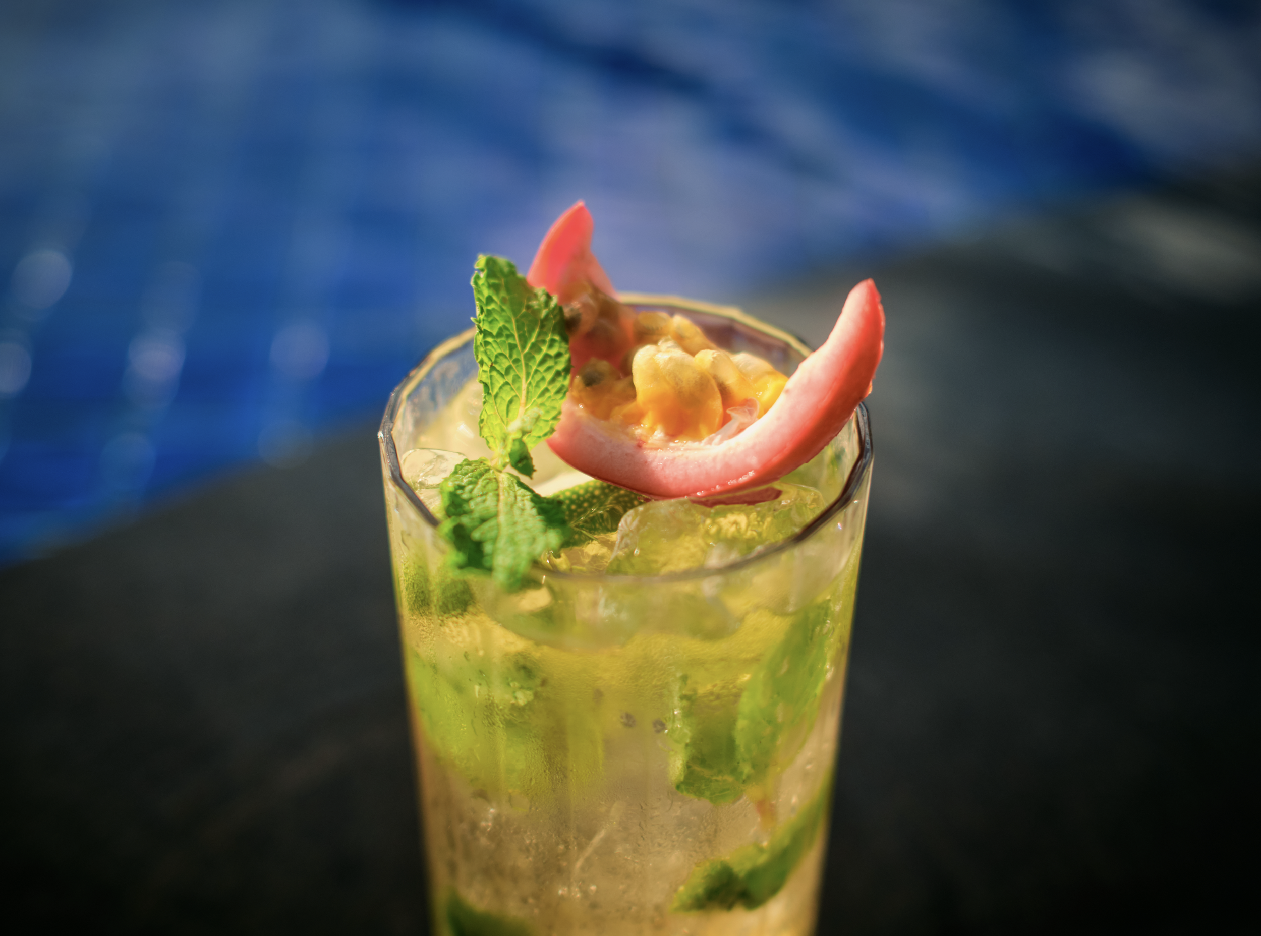 Close-up of a vibrant cocktail garnished with fresh mint leaves and slices of passionfruit in a tall glass.