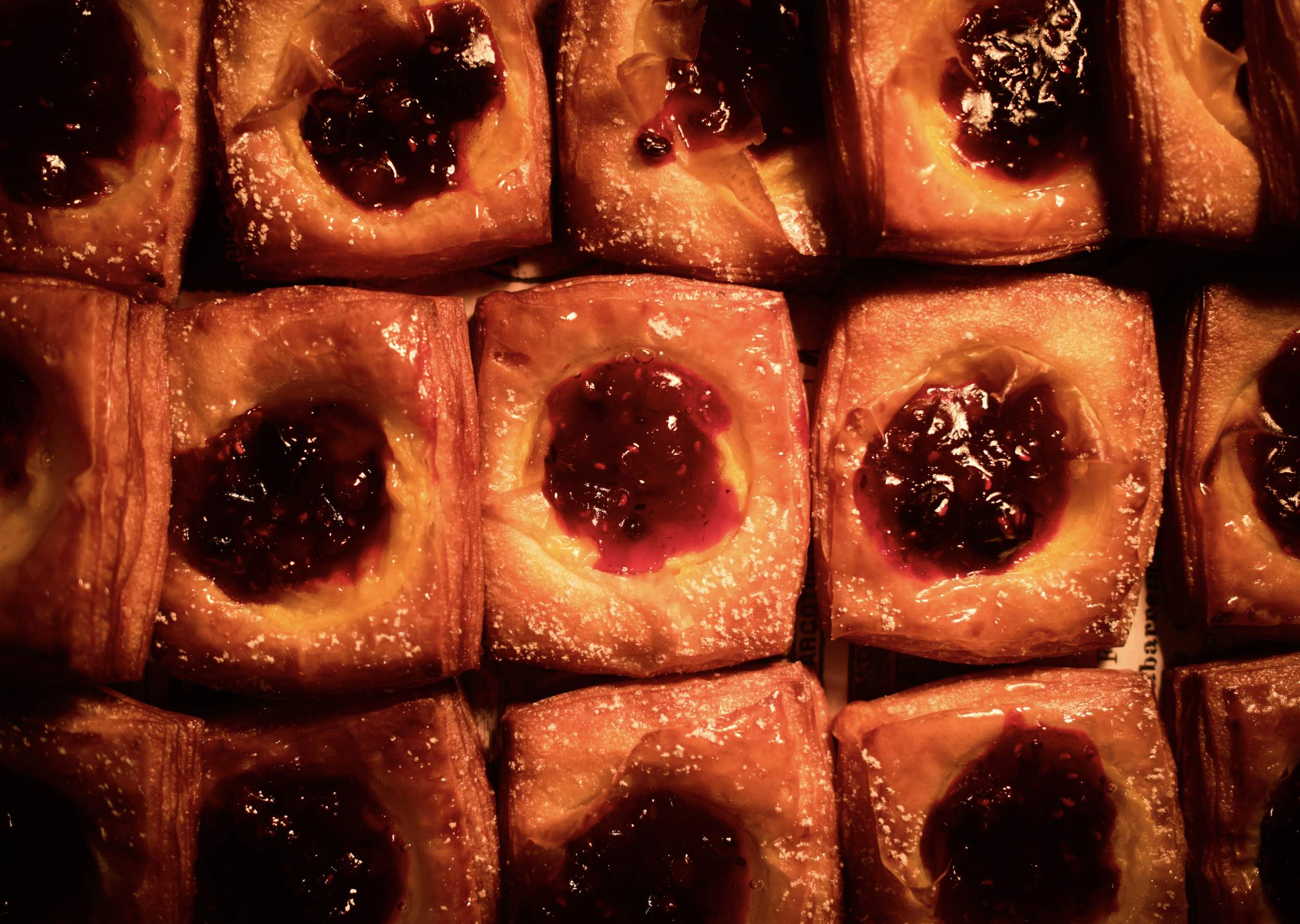 Close-up of square pastries with a fruit jam topping, arranged in rows.