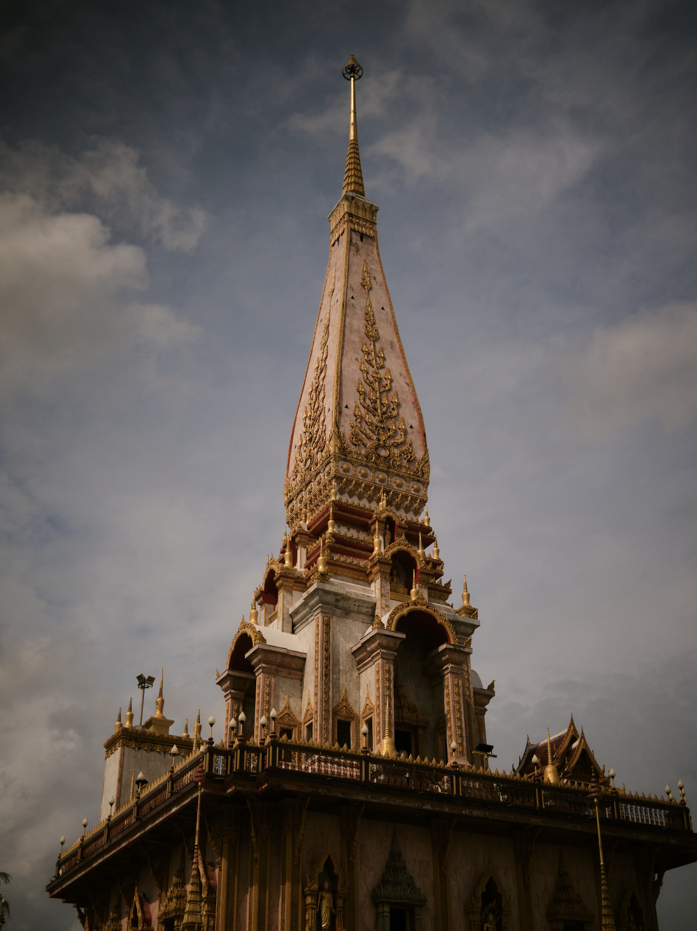 A tall, ornate Thai temple with a golden spire against a cloudy sky. Anemoia.