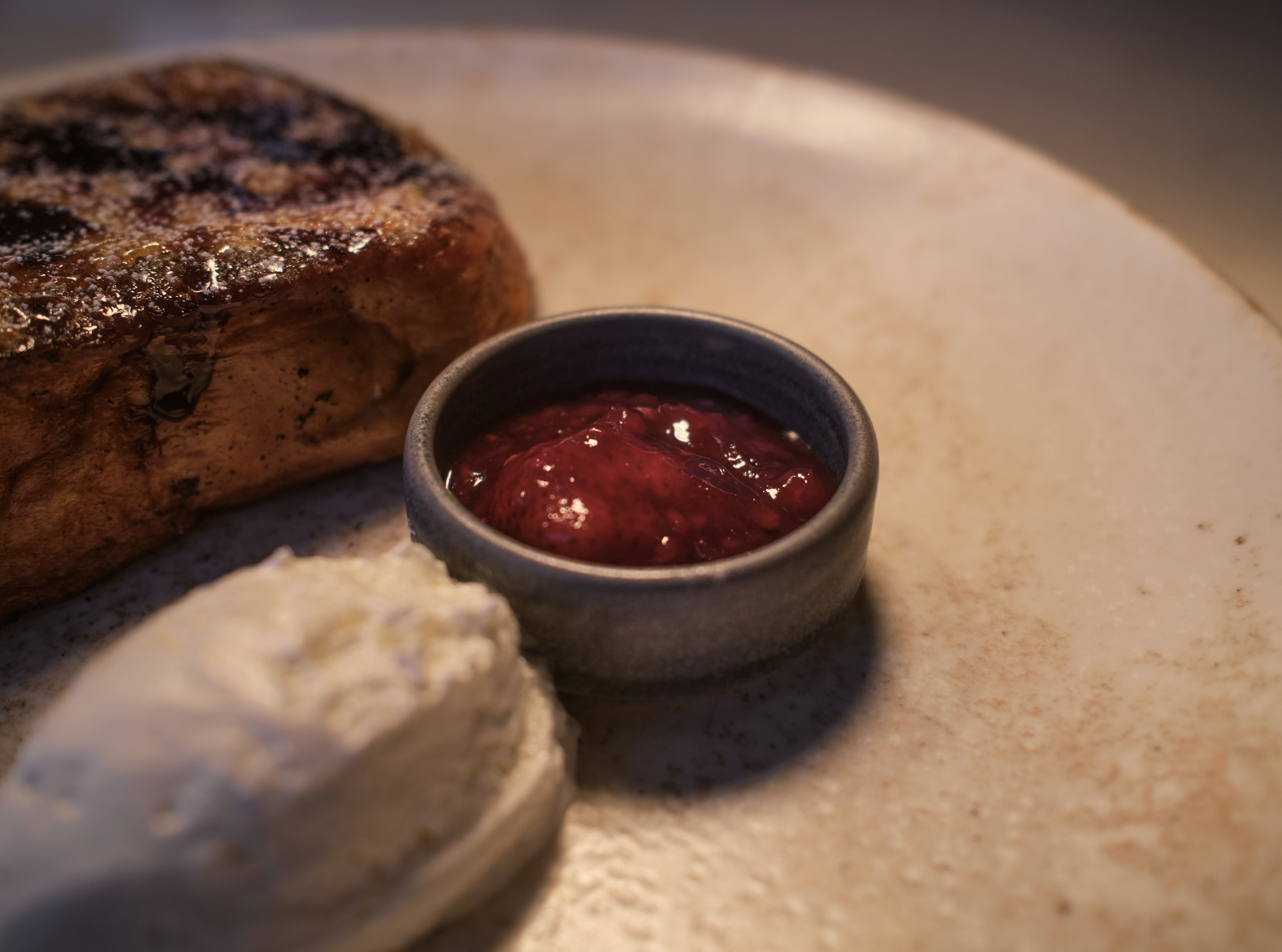 Close-up of a grilled steak with grill marks next to a small cup of dark red berry jam or sauce.