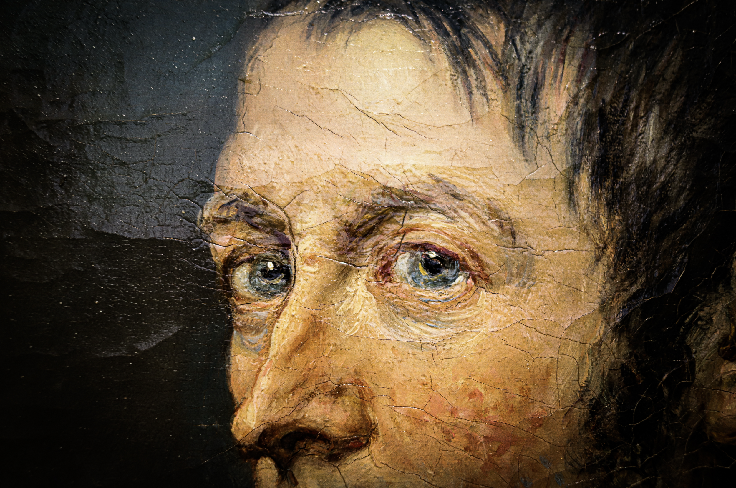 Close-up of an old, cracked oil painting of a person's face with blue eyes, partially visible hair, and detailed facial features.