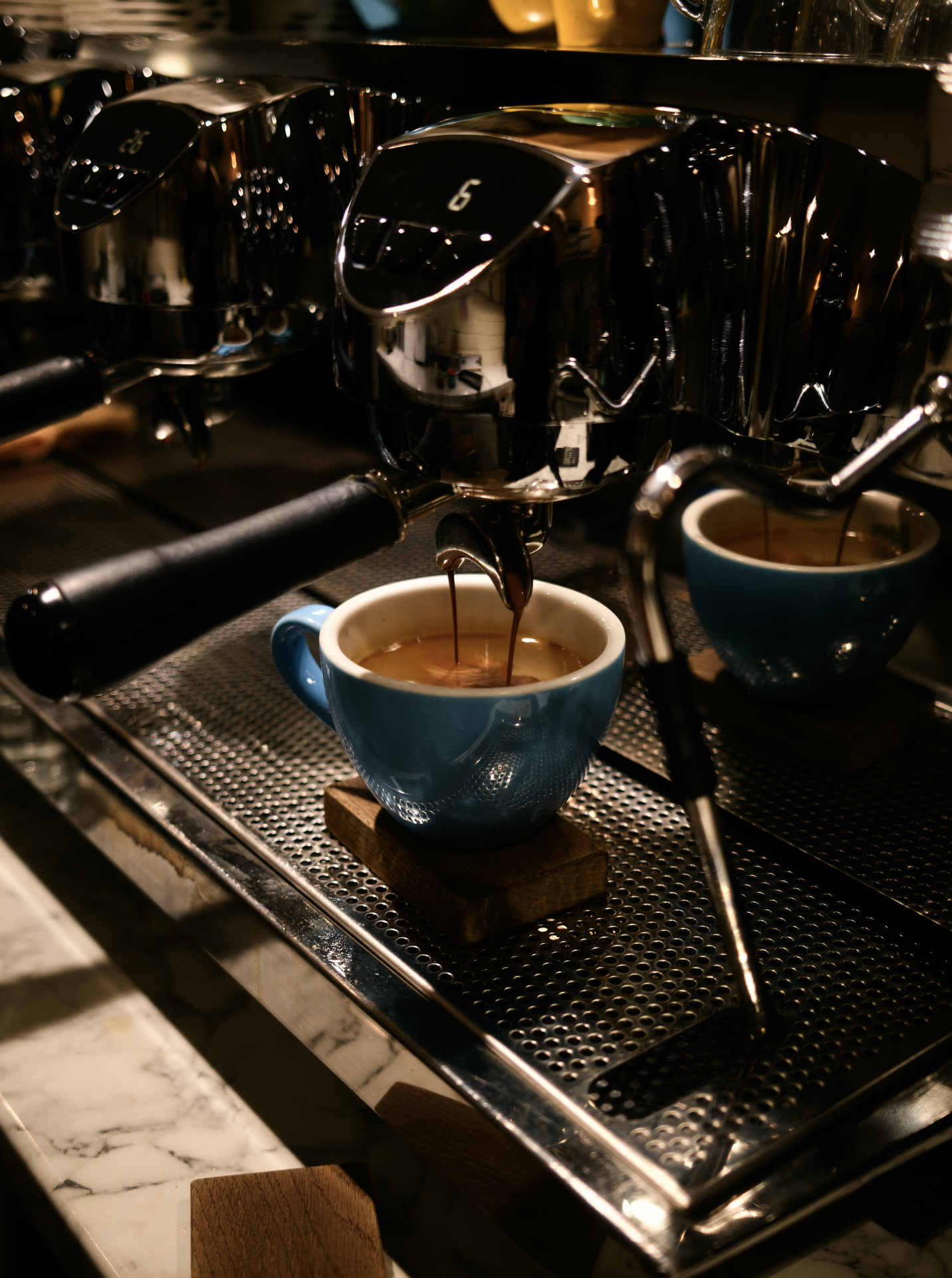 An espresso machine brewing coffee into two blue ceramic cups on a stainless steel counter.