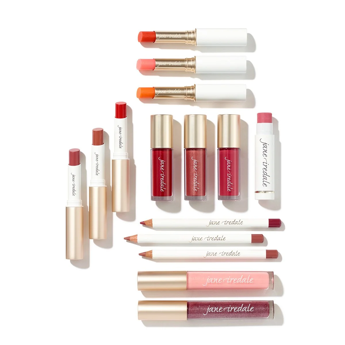 Collection of lipsticks, lip glosses, and lip balms in shades of red, pink, and nude by Jane Iredale, arranged on a white background.