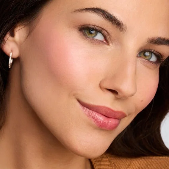 Close-up of a woman's face showing her with green eyes, earrings, and a subtle smile.