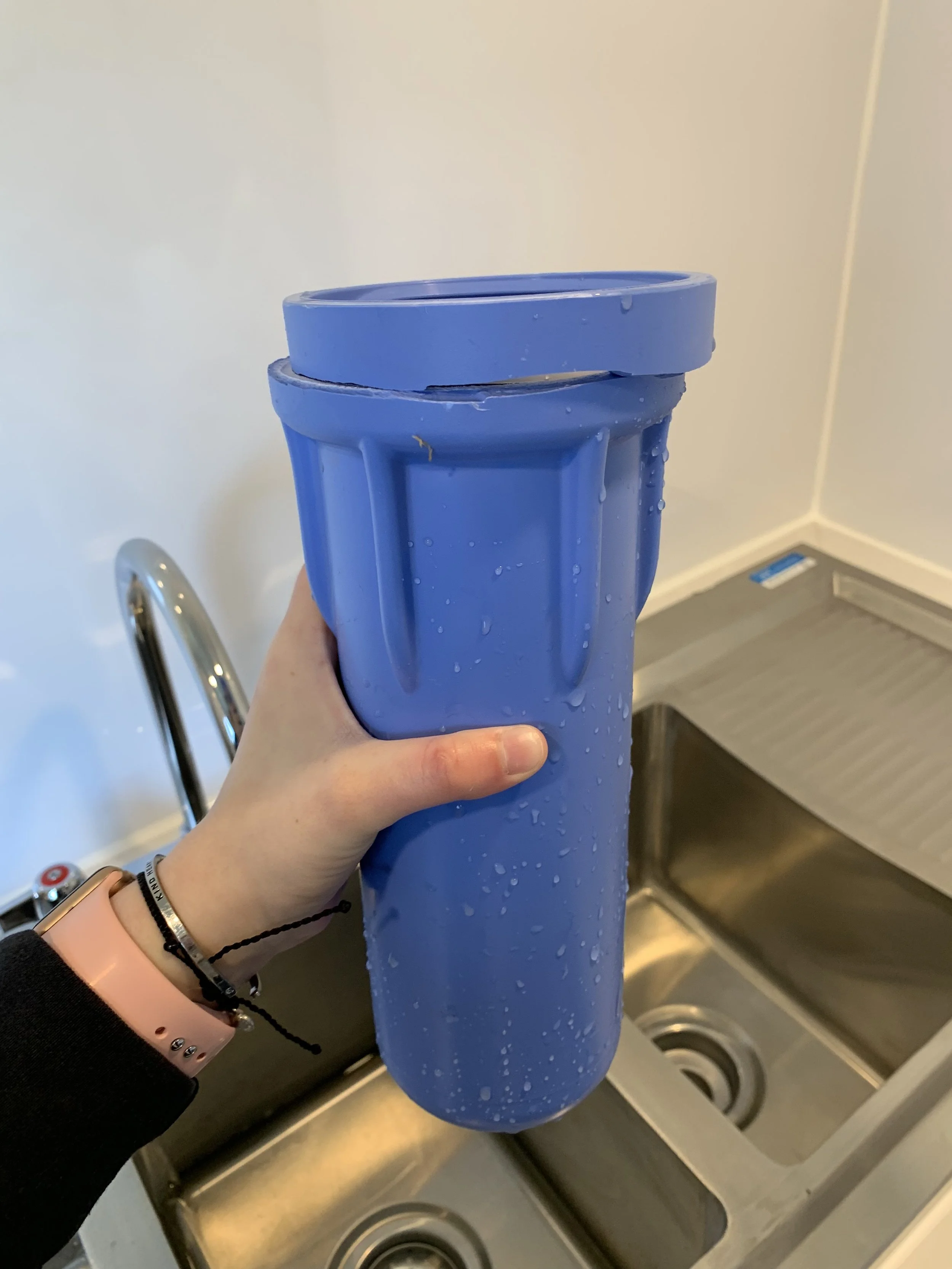 A hand holds a broken water filter housing which was damaged after water froze in it and cracked the housing. Water flooded the mobile unit when it was started up next.