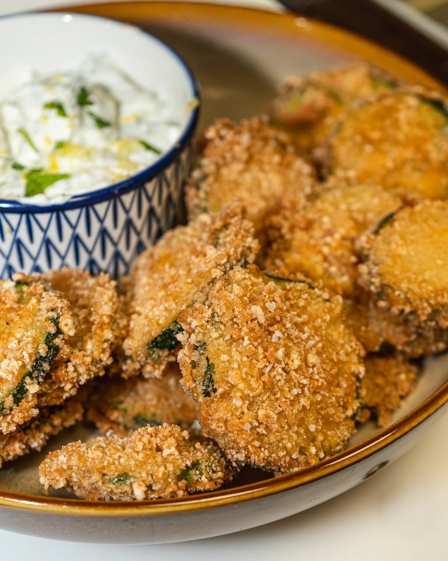 Crispy fried zucchini slices served on a plate with a creamy dipping sauce, photographed for Nisi Greek Kitchen + Bar.