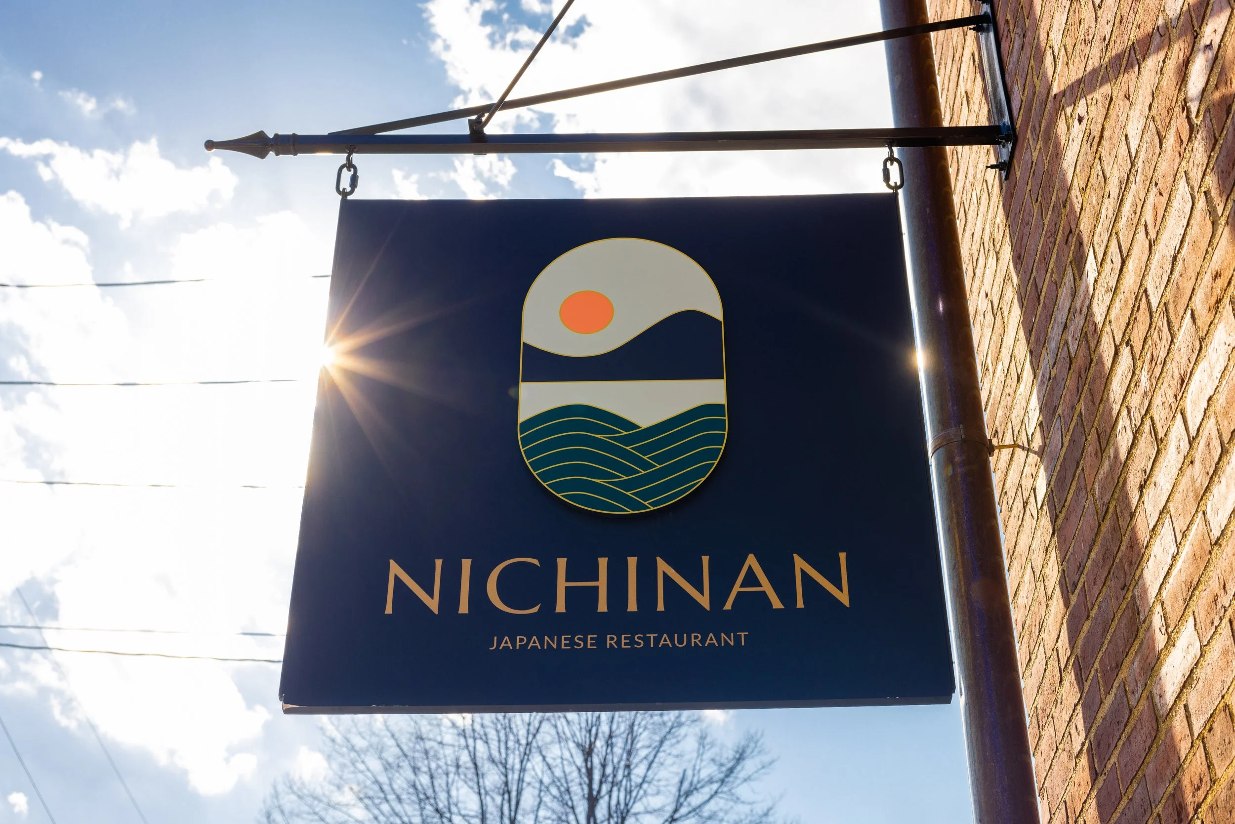 Outdoor sign for Nichinan Japanese Restaurant featuring a stylized landscape and sun logo.