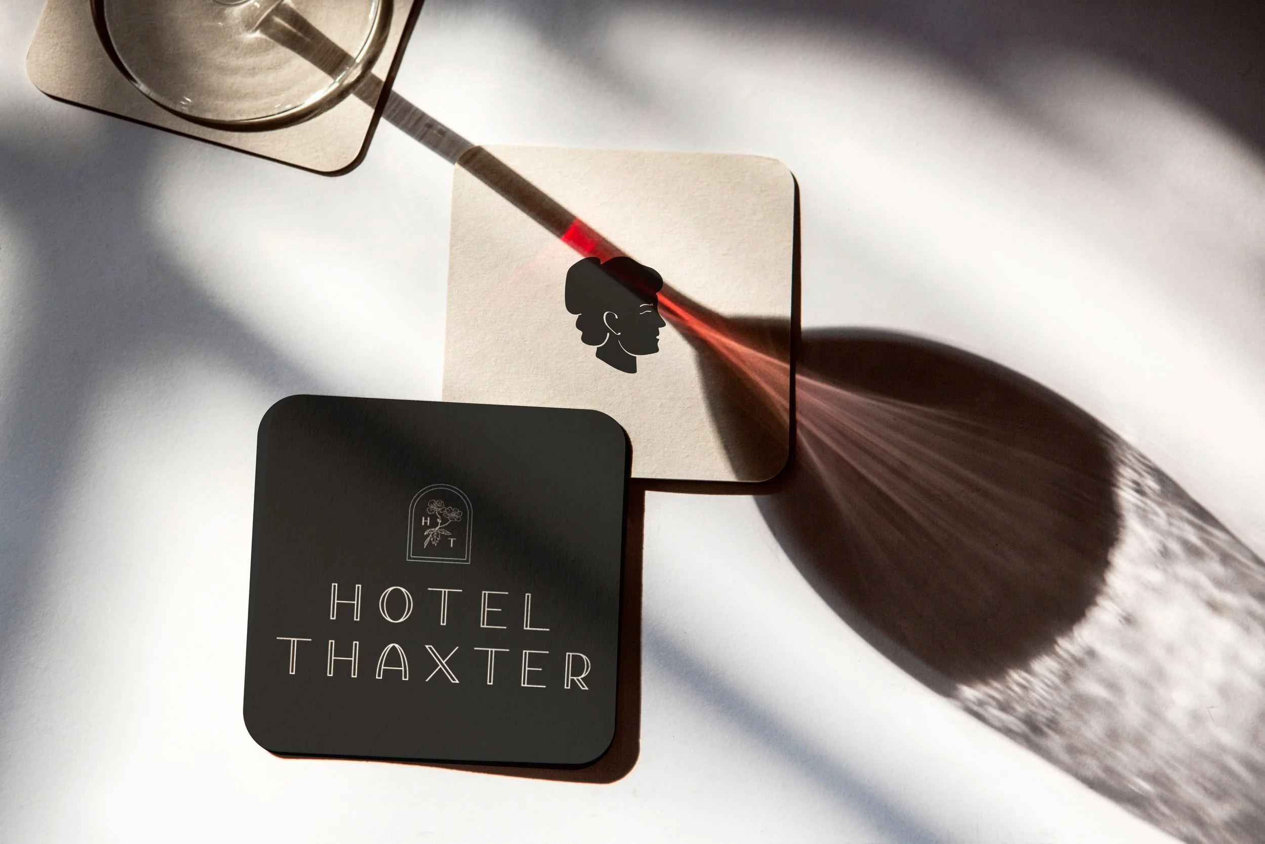Hotel Thaxter  branded coasters styled with soft shadows and plant silhouettes on a white surface.