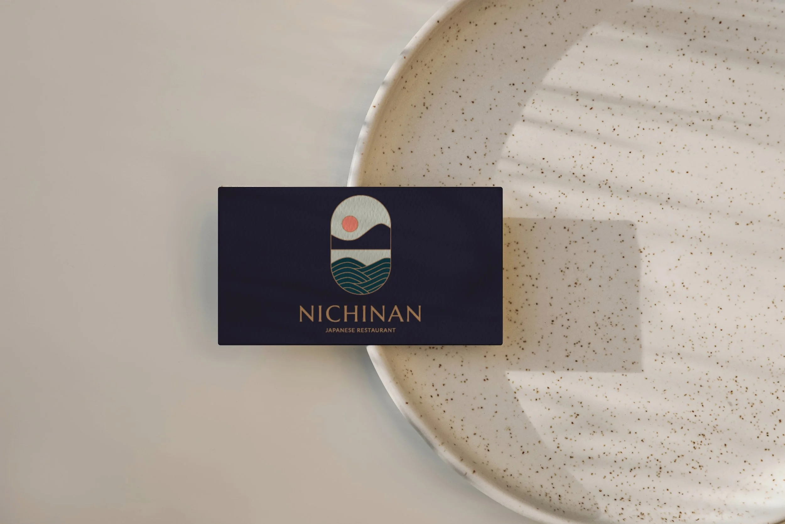 Dark navy branding card featuring the Nichinan Japanese Restaurant logo and gold typography on a light surface.