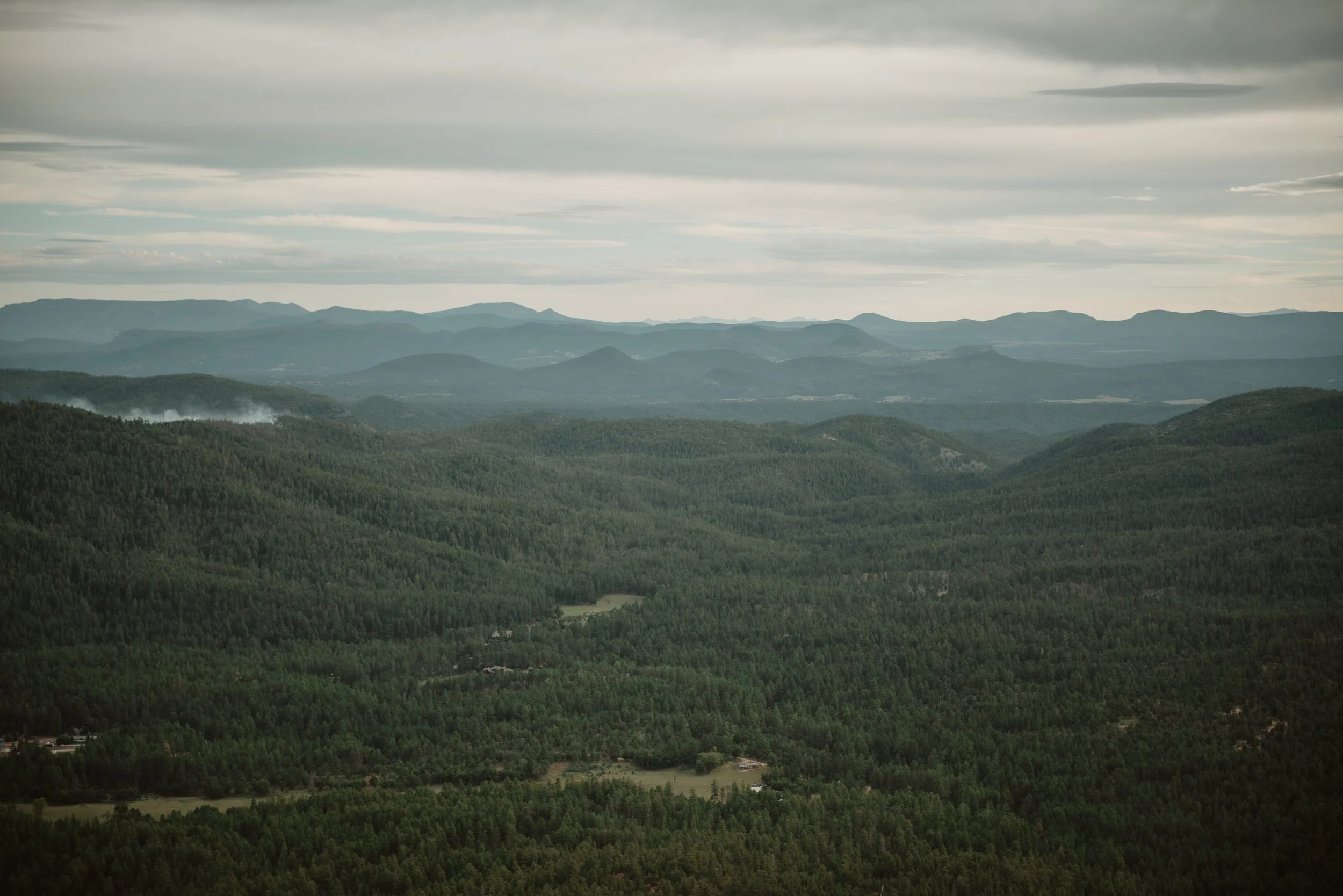 Aerial view of a vast forested landscape with rolling hills and distant mountains under an overcast sky.