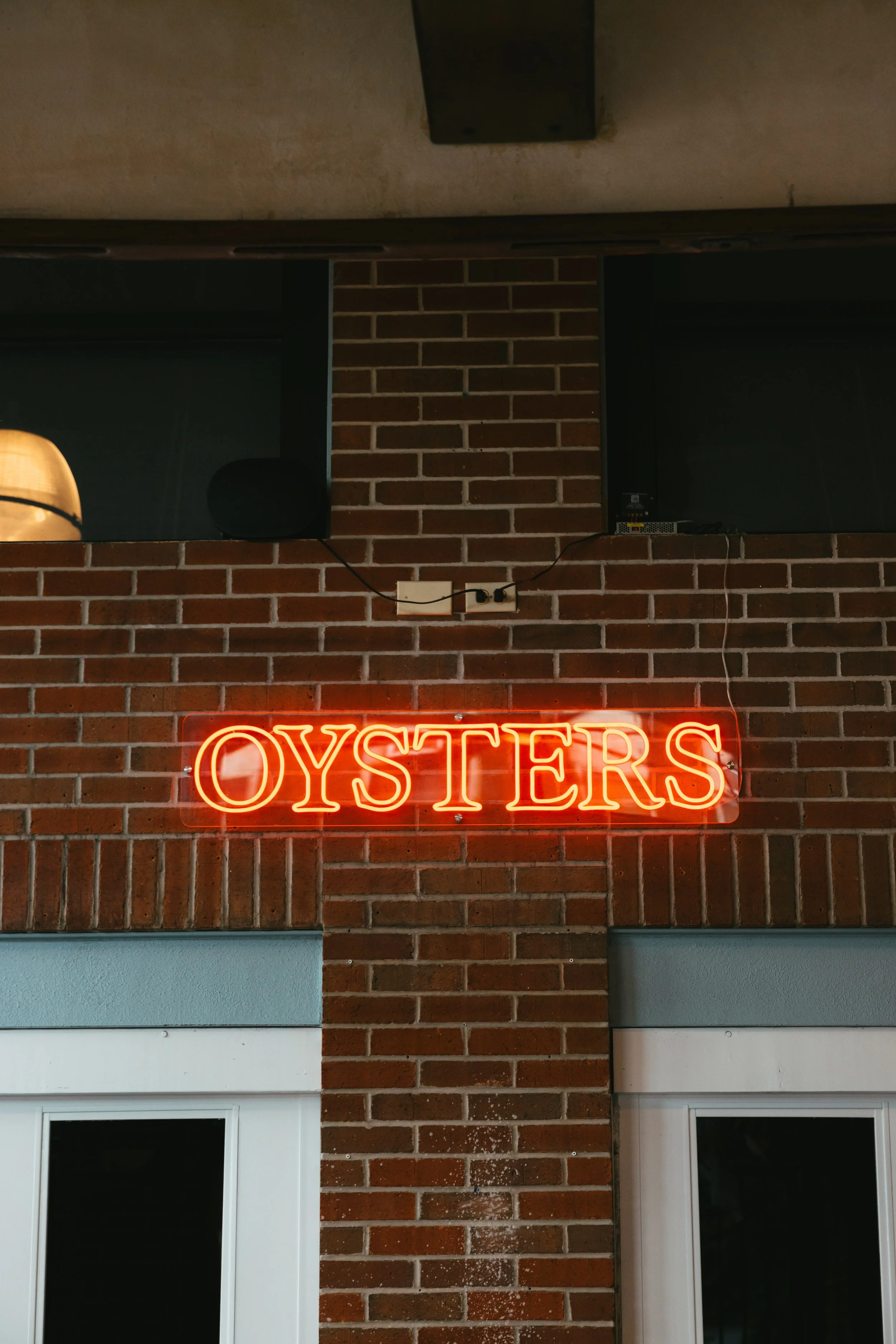 Neon sign that says "OYSTERS" mounted on a brick wall.