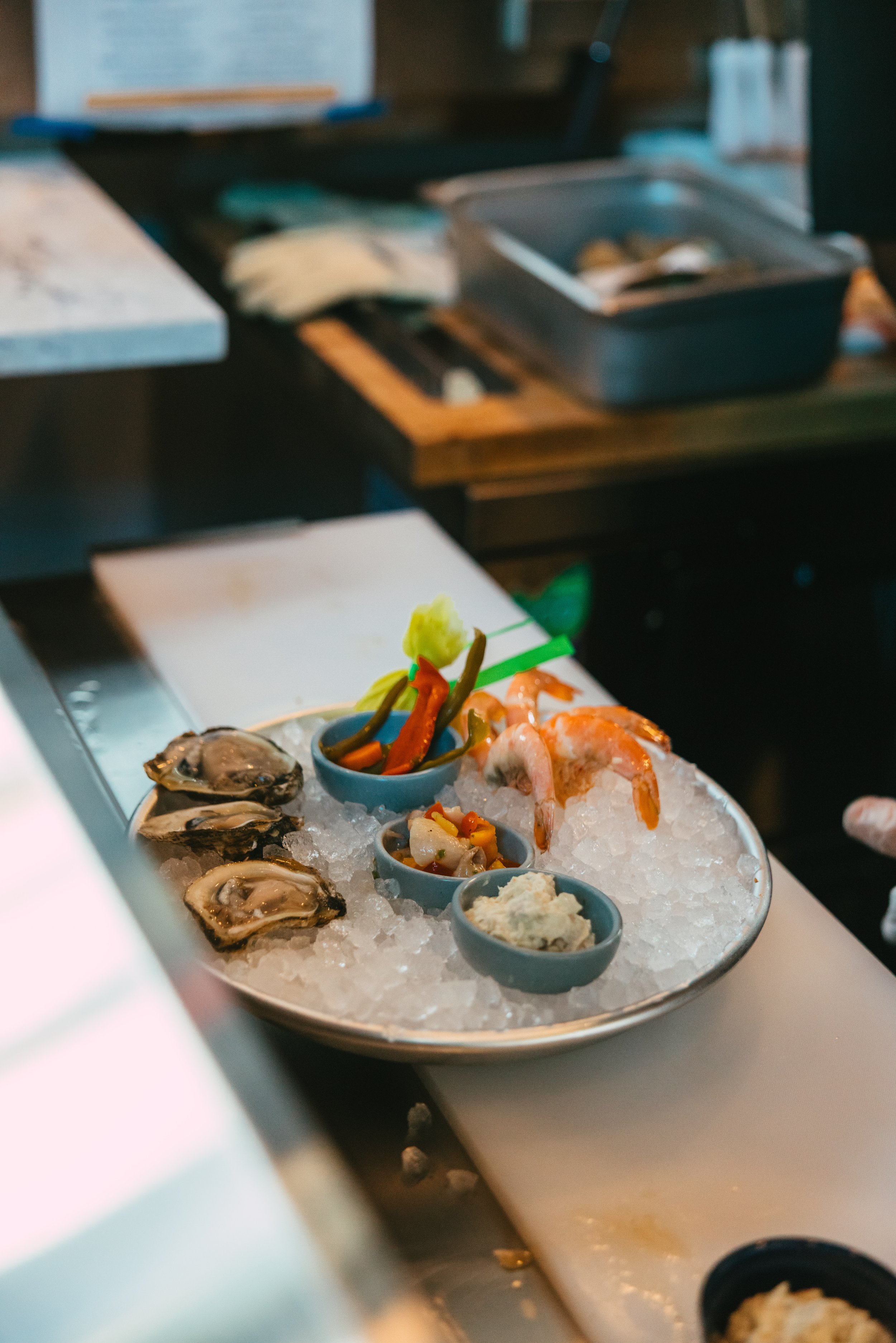 Plate of oysters, shrimp, and small bowls of sauces and garnishes on ice at a seafood restaurant.