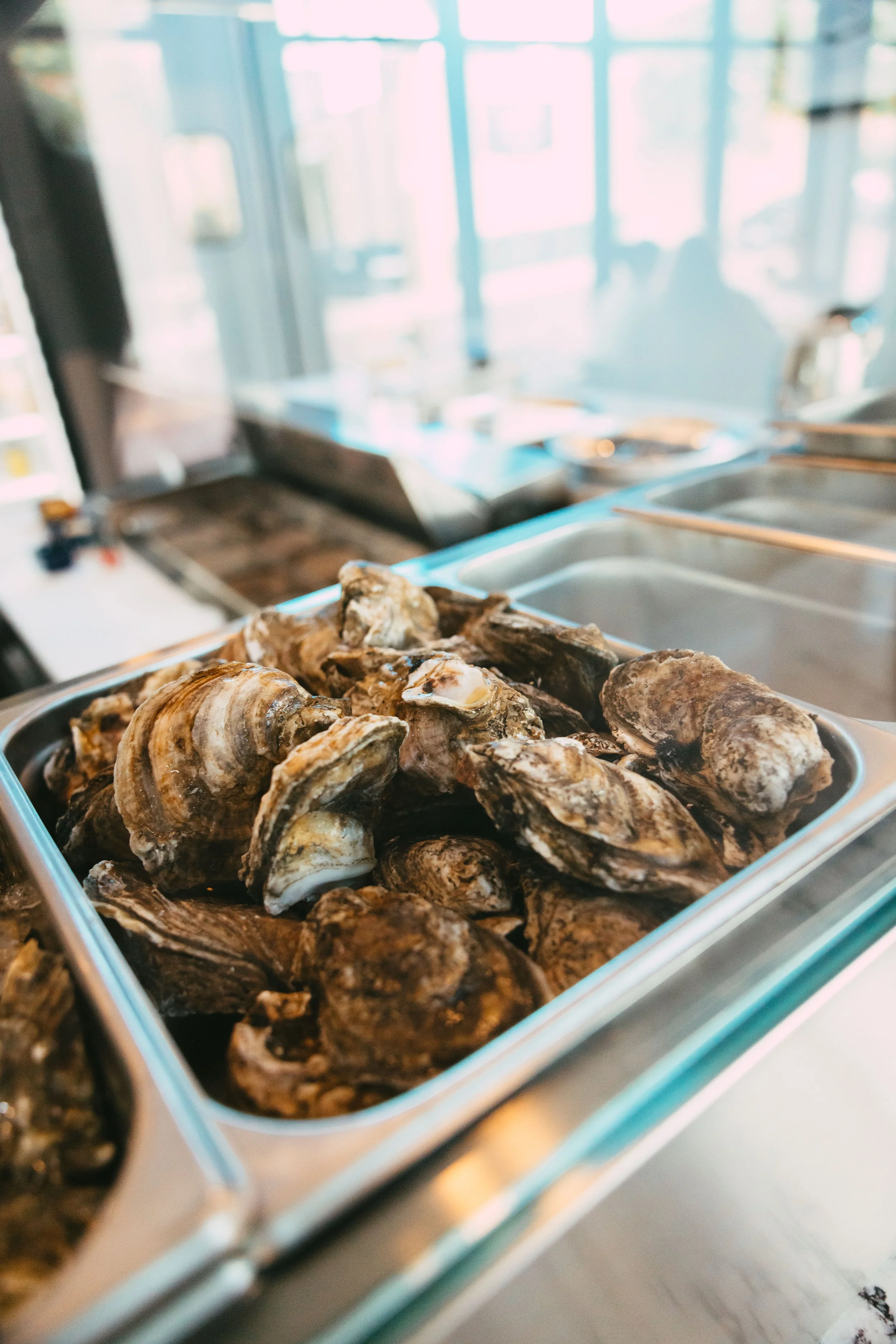 A metal tray filled with raw oysters on ice at a seafood restaurant or market.