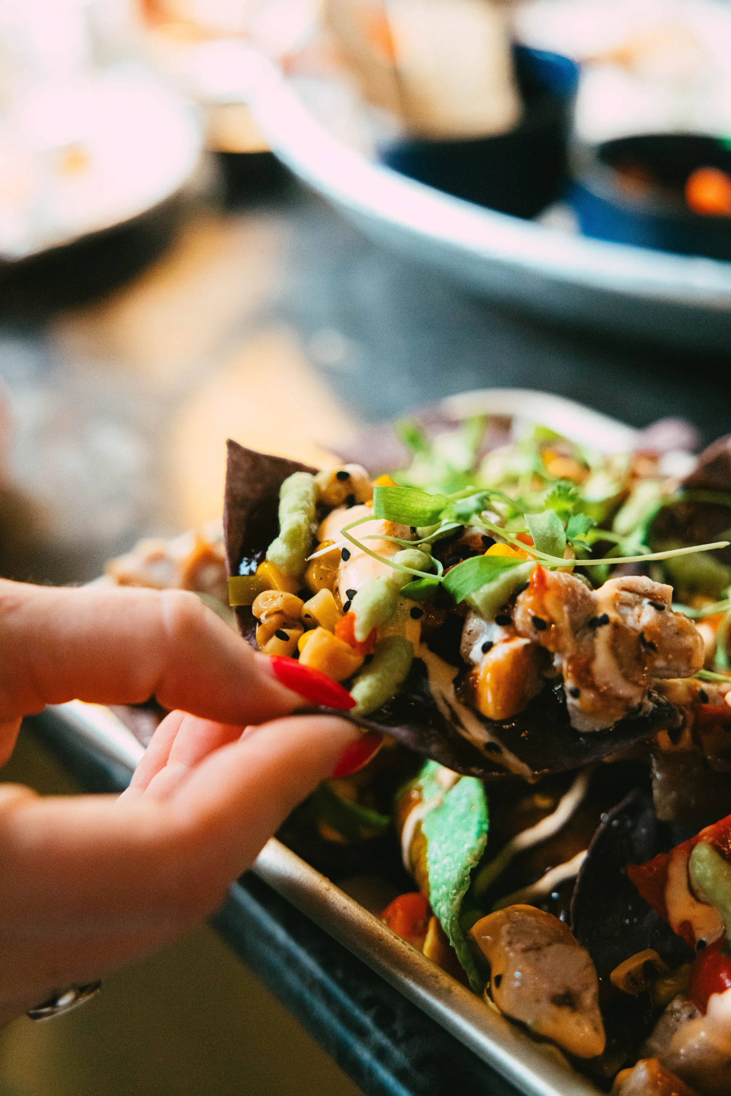 Close-up of a hand holding a crispy taco with various colorful toppings including corn, greens, and sauces.