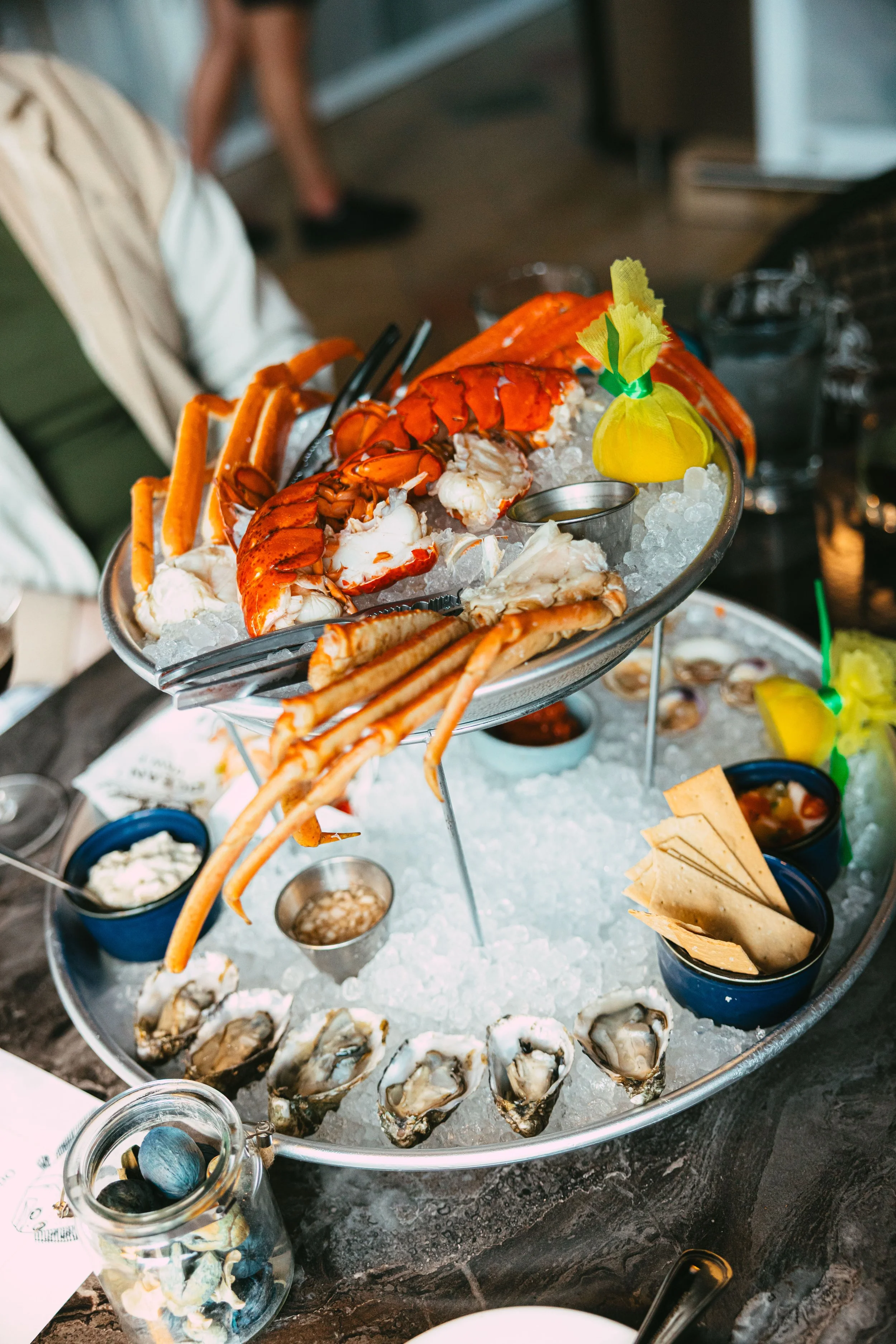 Lobster, crab, oysters, and other seafood on a bed of ice at a seafood platter with sauces and lemon garnishes.