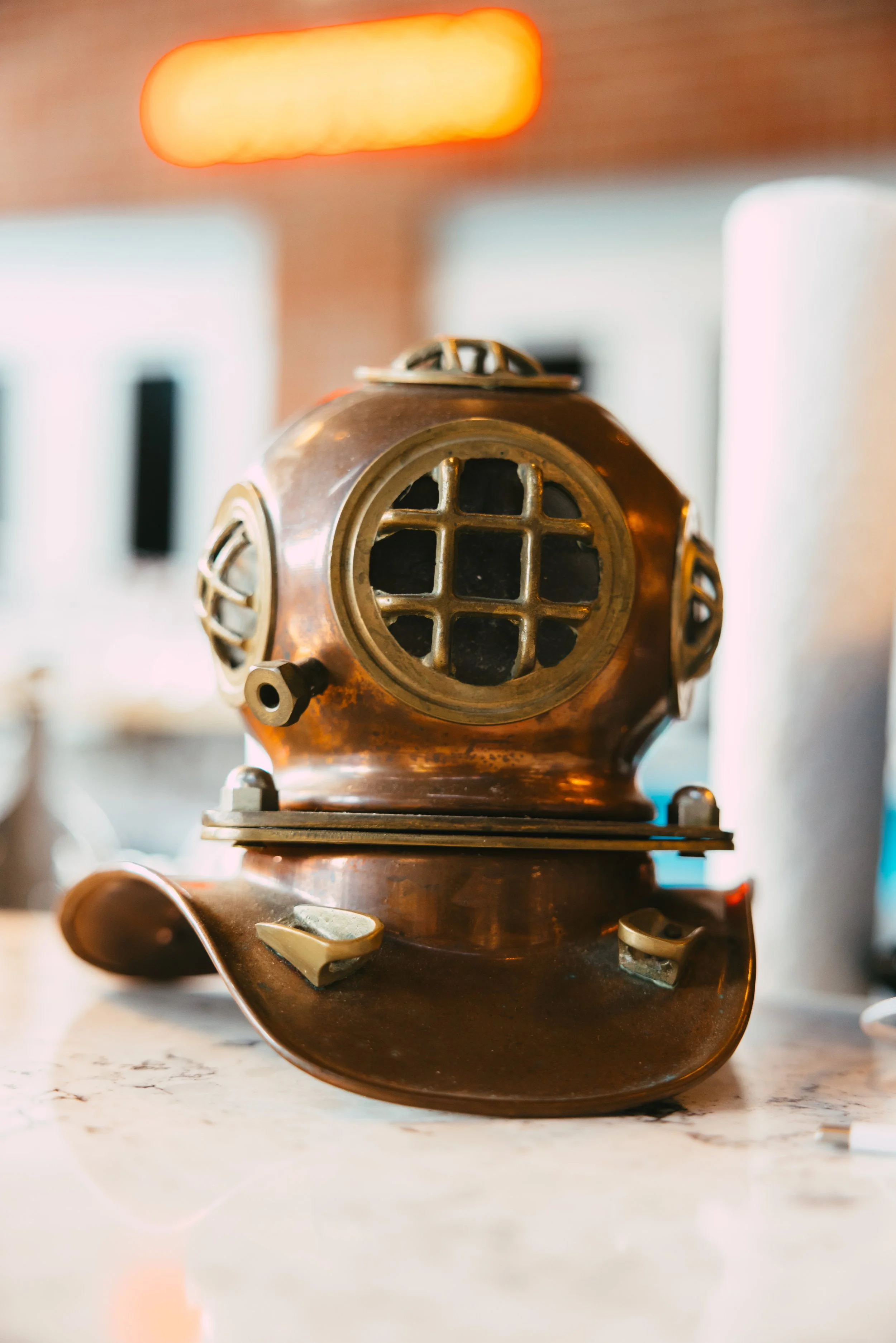 A vintage copper diving helmet with a grid window in the front, placed on a white marble surface.