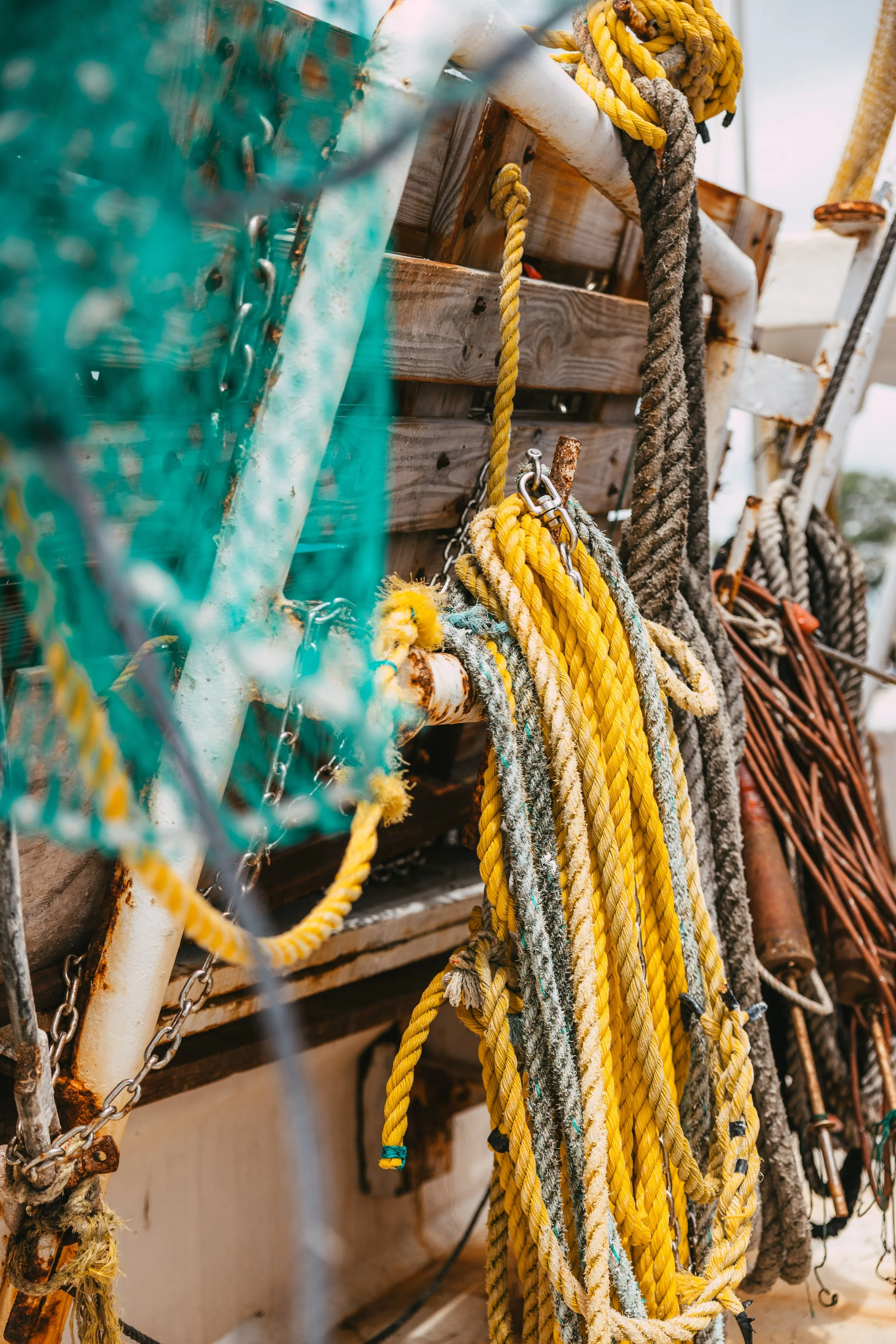 Boats with coiled ropes hanging on a wooden rack, some ropes are yellow, others are brown or gray, and a turquoise net in the foreground.