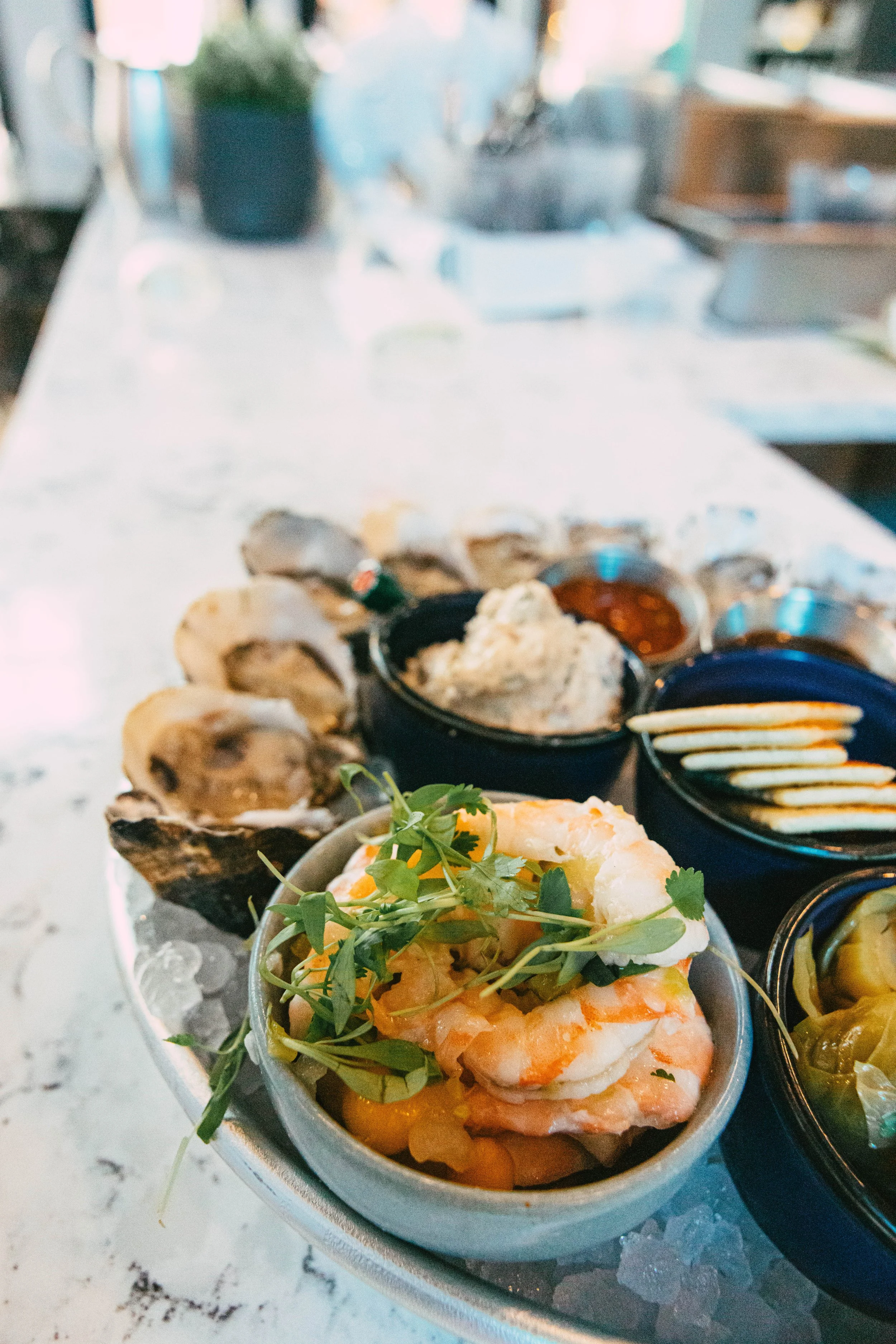 A seafood platter with shrimp, oysters, and various sauces on a white marble countertop.