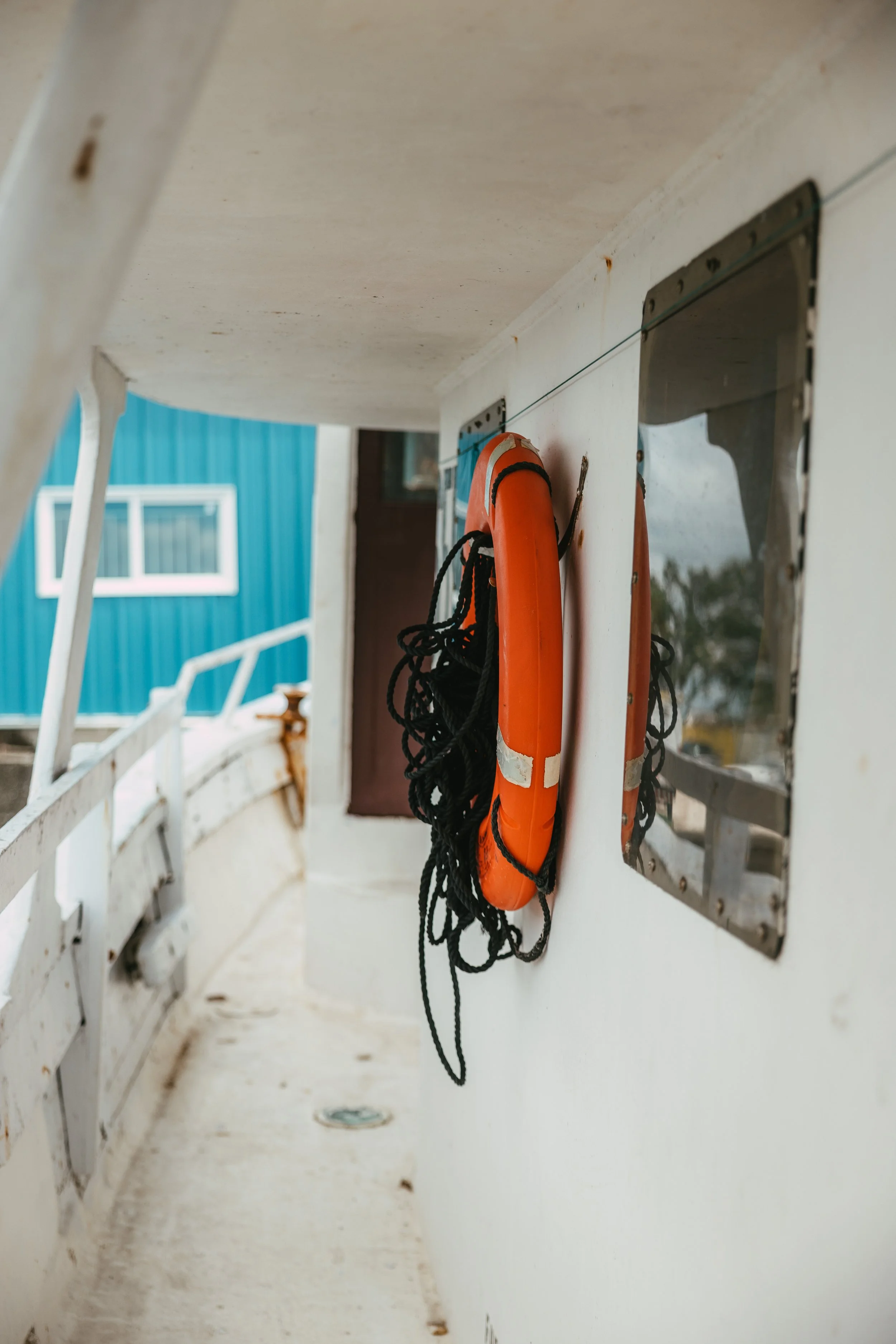 Close-up of a white boat wall with a mounted orange life preserver with black rope, next to a rectangular window with rounded edges.