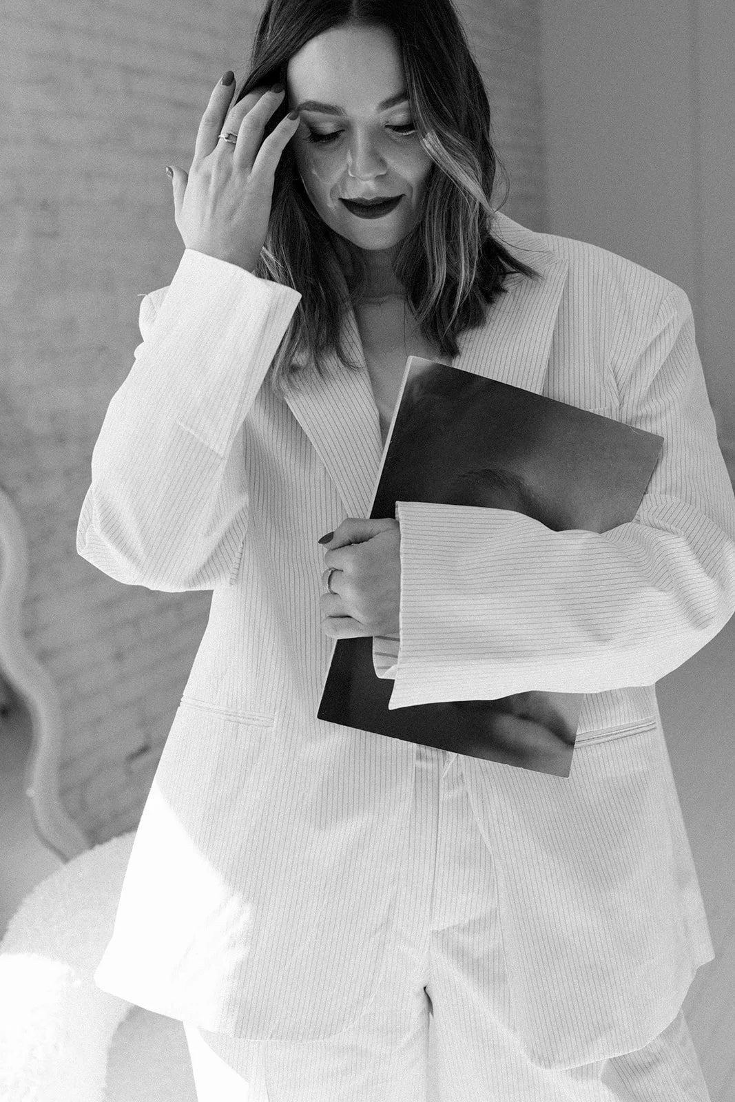 Black and white photo of a woman in a suit holding a folder, touching her forehead with her other hand.