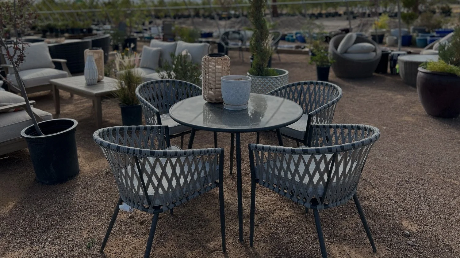These four woven lawn chairs surround a decorated circular table on a gravel landscape, available at Garden Center of Las Cruces, New Mexico.