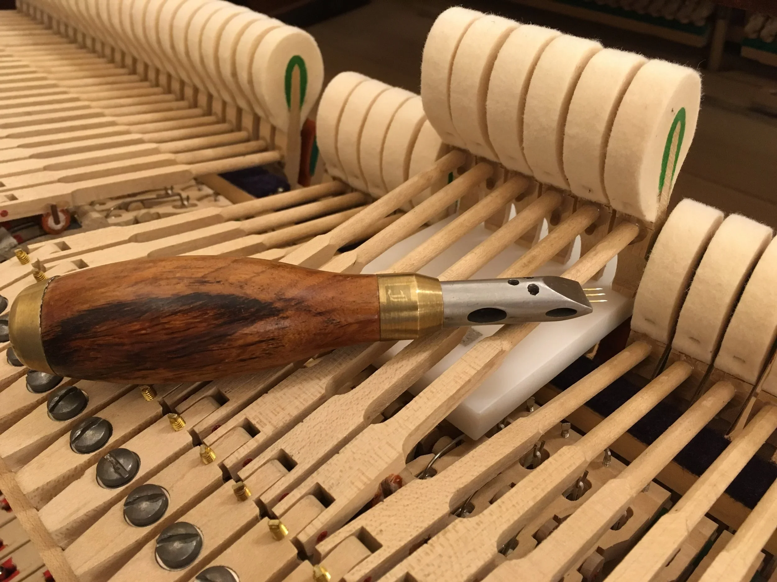 Close-up of piano hammer mechanism with a tuning or repair tool placed on the wooden frame.