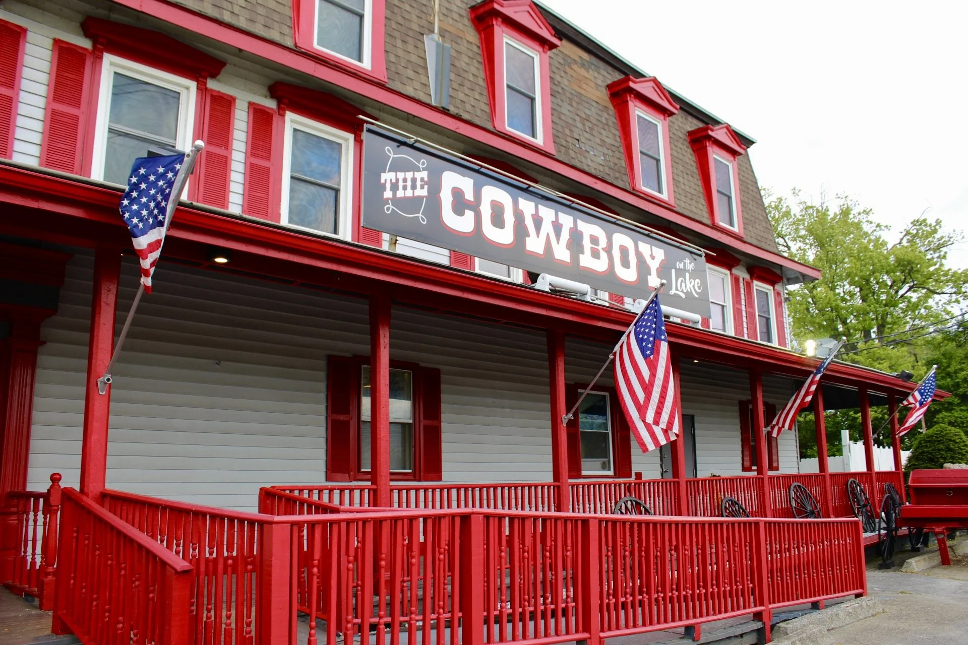 Red and white building with a sign that reads 'The Cowboy on the Lake,' decorated with American flags.