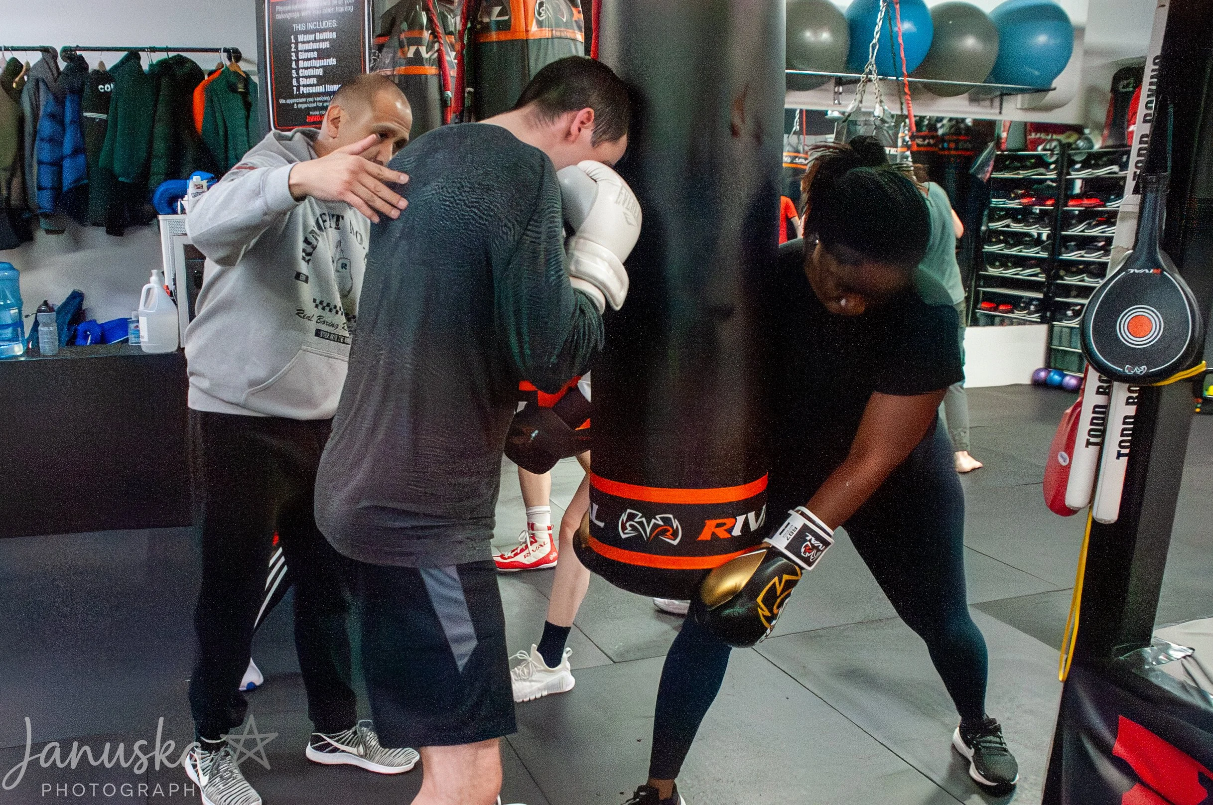 A group of people in a gym, with a boxer in gear being attended to by two trainers or coaches.