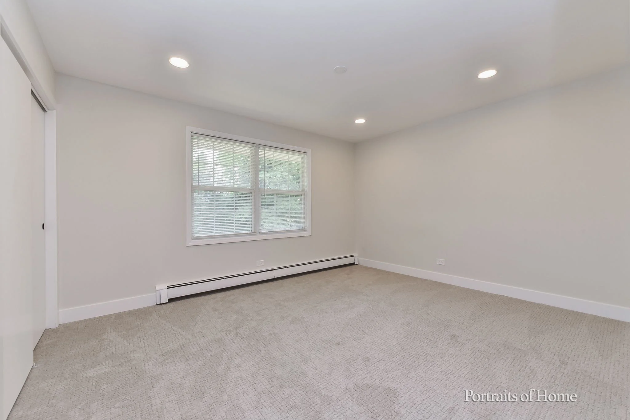 Empty room with beige carpet, white walls, a window with blinds, and ceiling lights.