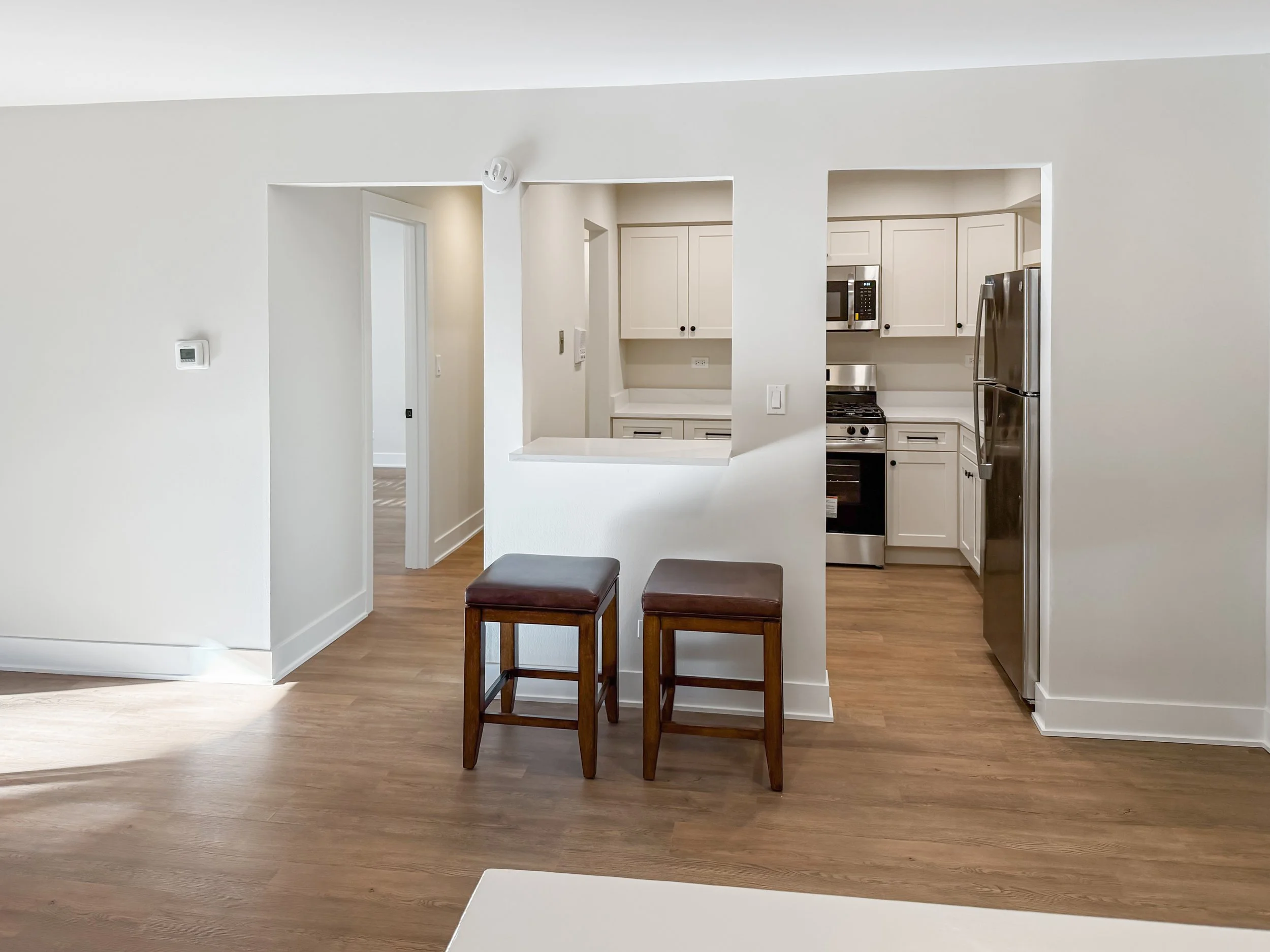 Modern kitchen with white cabinets, stainless steel appliances, and a breakfast bar with two wooden stools.