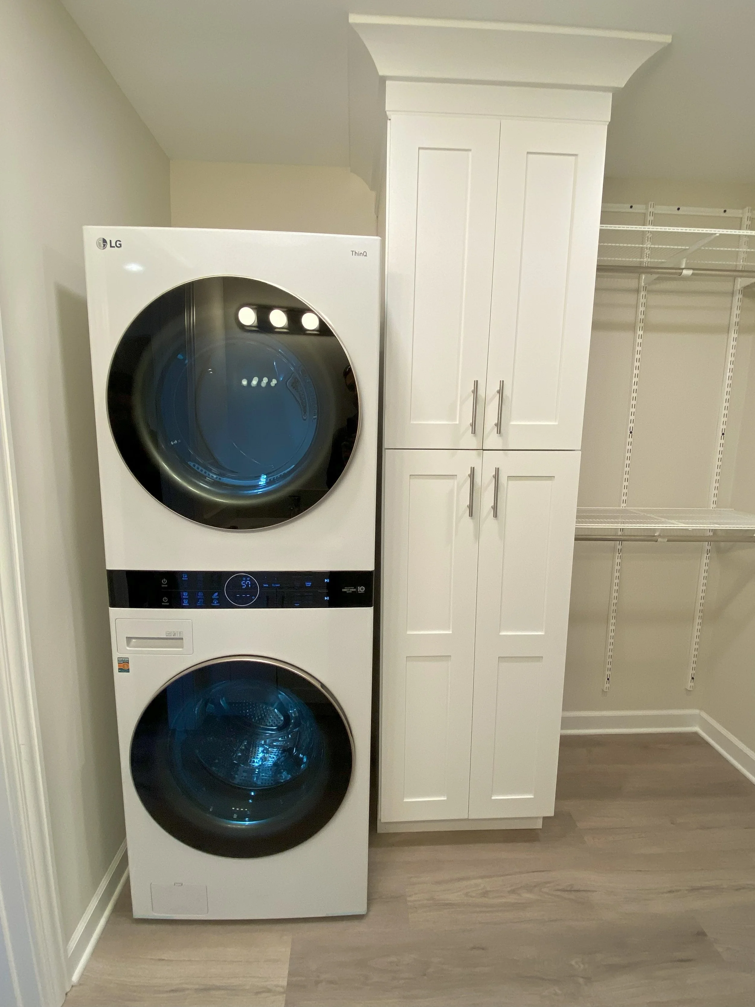 A laundry room with a stacked LG washer and dryer next to a white storage cabinet and empty wire shelving.