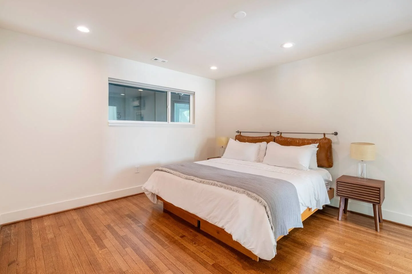 A bedroom with a bed, two nightstands with lamps, a window, and wooden flooring.