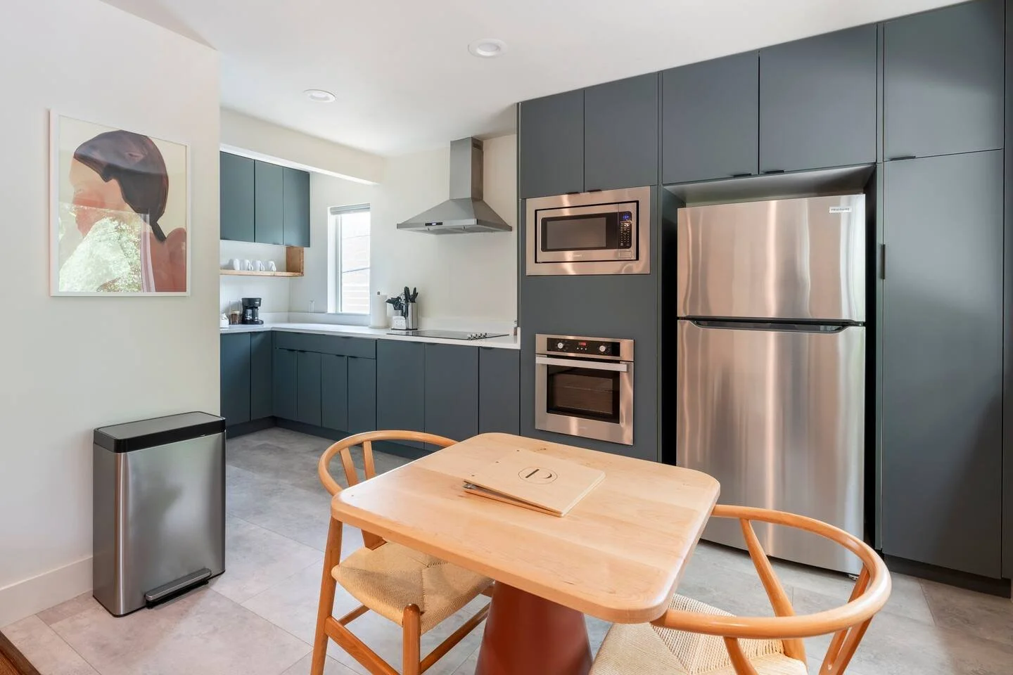 Modern kitchen with gray cabinetry, stainless steel appliances, and a small wooden dining table with chairs.