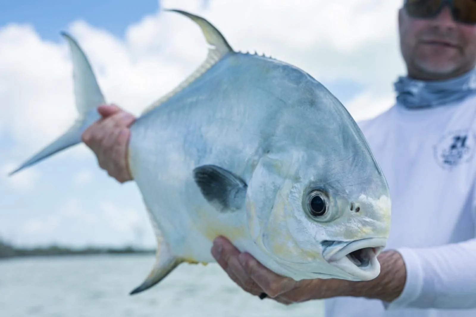 Person håller en stor permit vid vattnet i Mexiko under molnigt väder under en fiskeresa med Outside Travels.