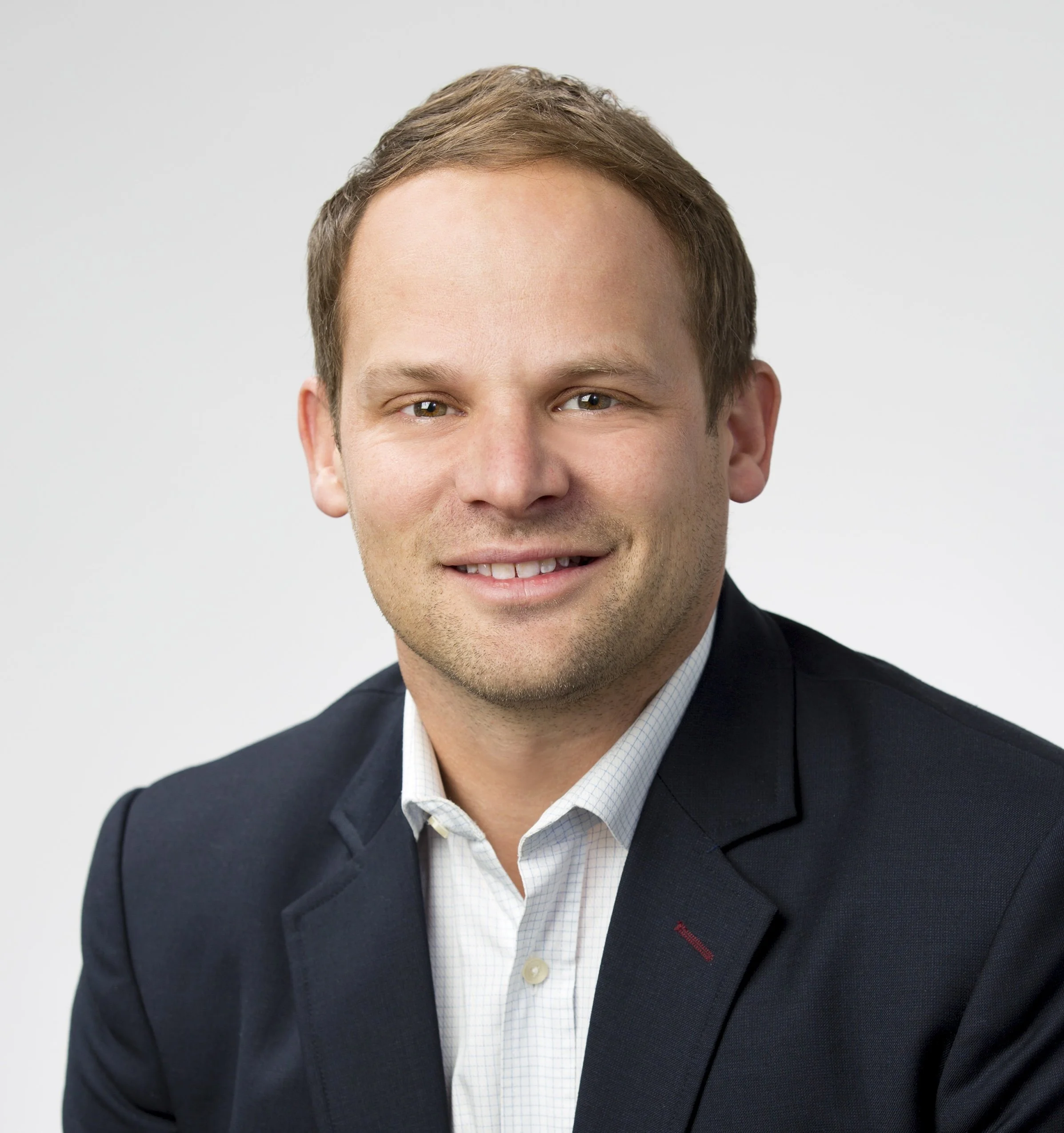 Close-up of a smiling man in business attire against a plain light background.