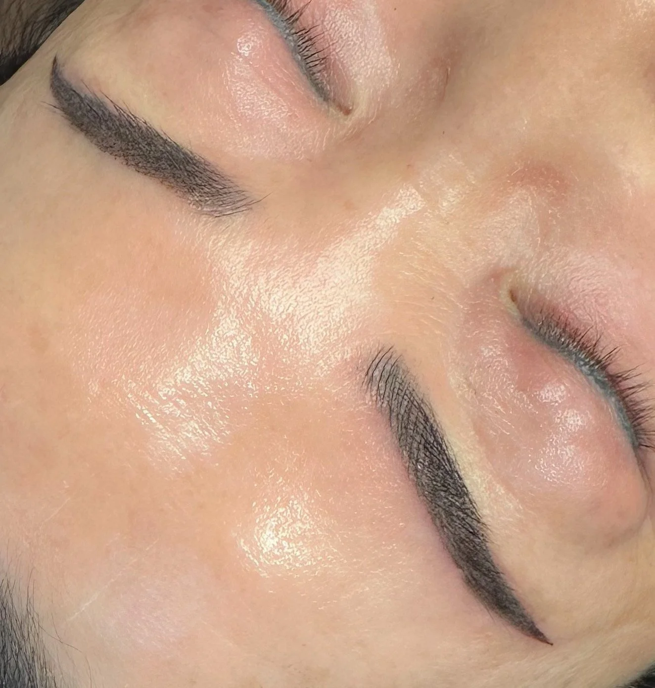 Close-up of a person's face with closed eyes, showing well-groomed eyebrows and smooth skin.