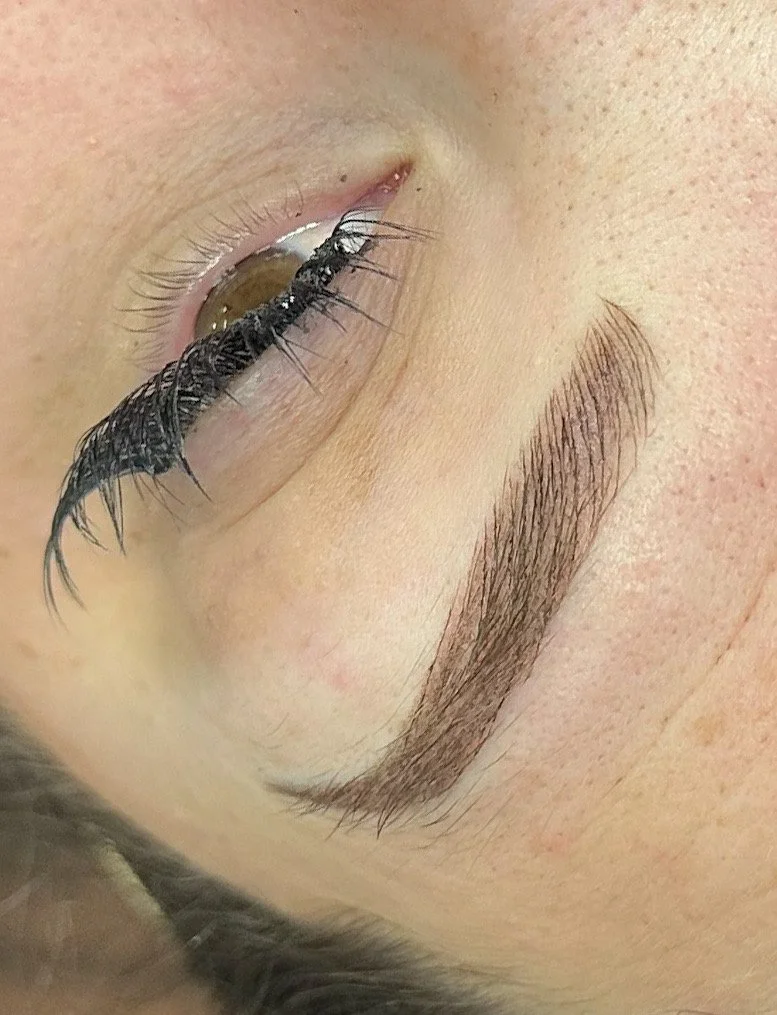 An eyelash curler pressing on a person's closed eye with long eyelashes and well-defined eyebrows.