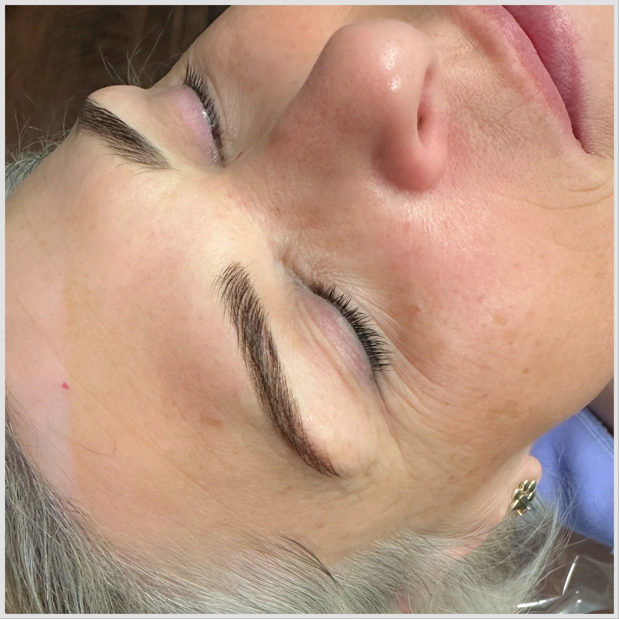 Close-up of a woman's face with closed eyes, showcasing well-groomed eyebrows and clear skin, lying down with her head tilted to the side.