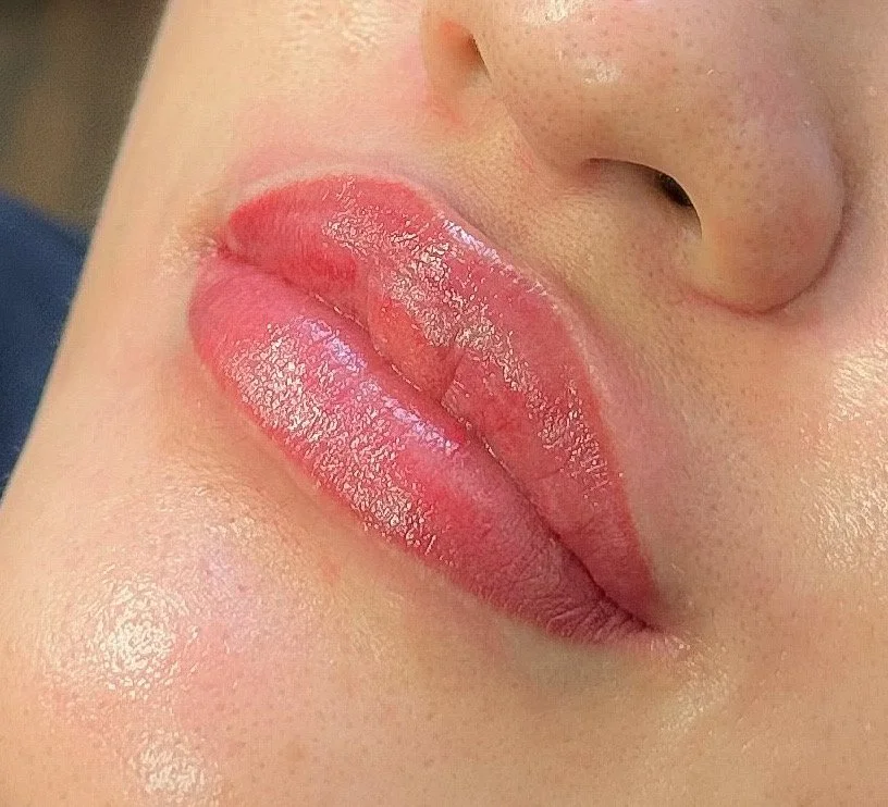 Close-up of a person's lips with glossy light pink lipstick near the nose.