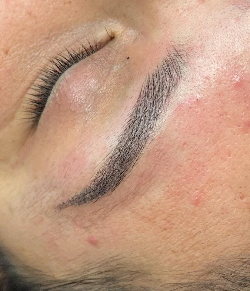 Close-up of a closed eye showing long eyelashes, a groomed eyebrow, smooth skin, and some small skin blemishes.